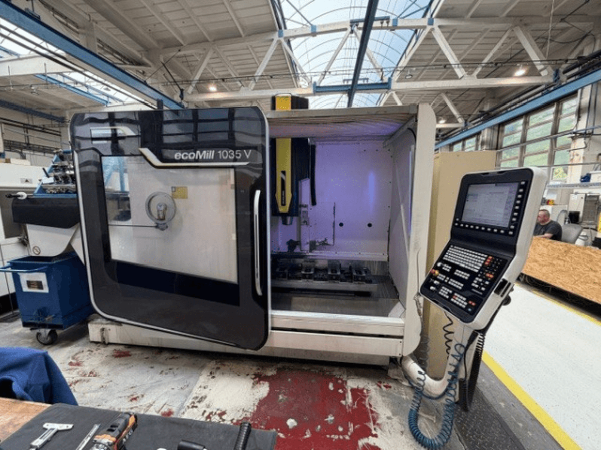DMG MORI ecoMill 1035V vertikālā apstrādes centra skats no priekšpuses ar atvērtām durvīm, kurā redzams vadības panelis un darba zona iekārtas iekšpusē.