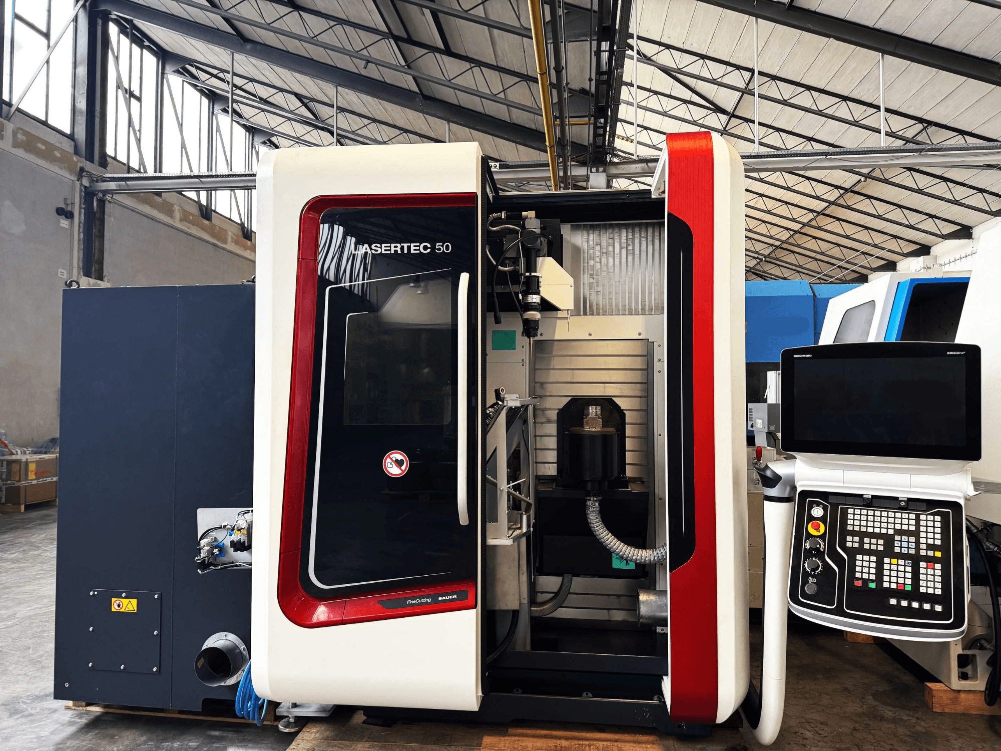 LaserTec 50 CNC mašīna no sānu skata, ar melnbaltu vadības paneli, redzamu instrumentu turētāju un rūpniecisku iestatījumu.