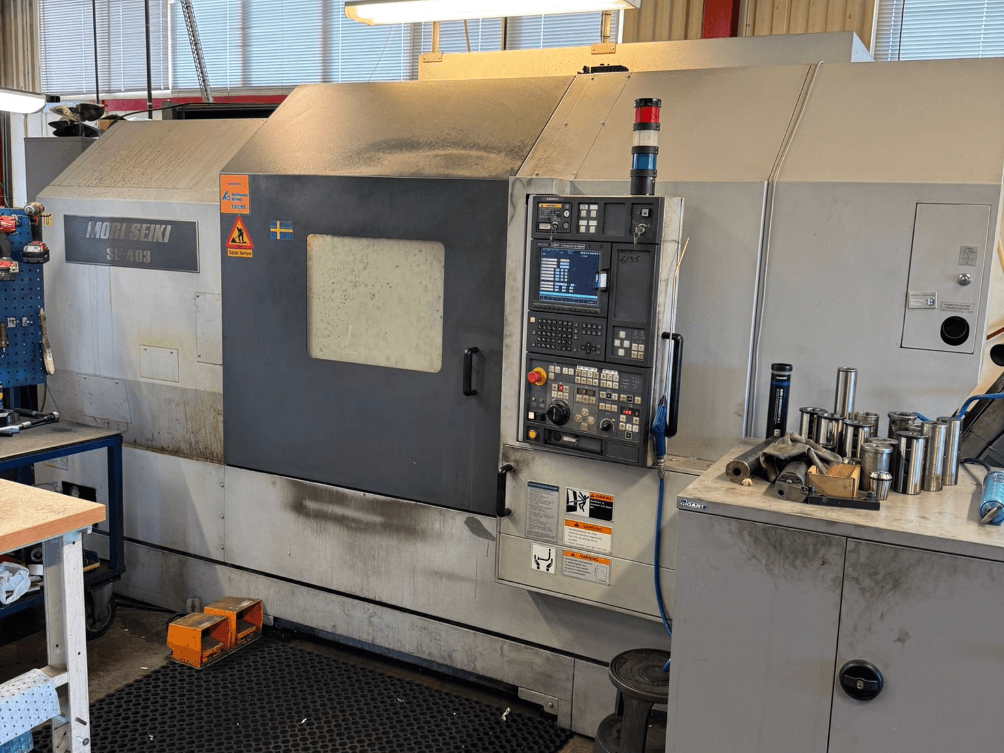 MORI SEIKI SL-403BMC/800 horizontālās virpošanas mašīna darbnīcā, redzams vadības panelis un tuvumā esošie instrumenti, skats no sāniem.