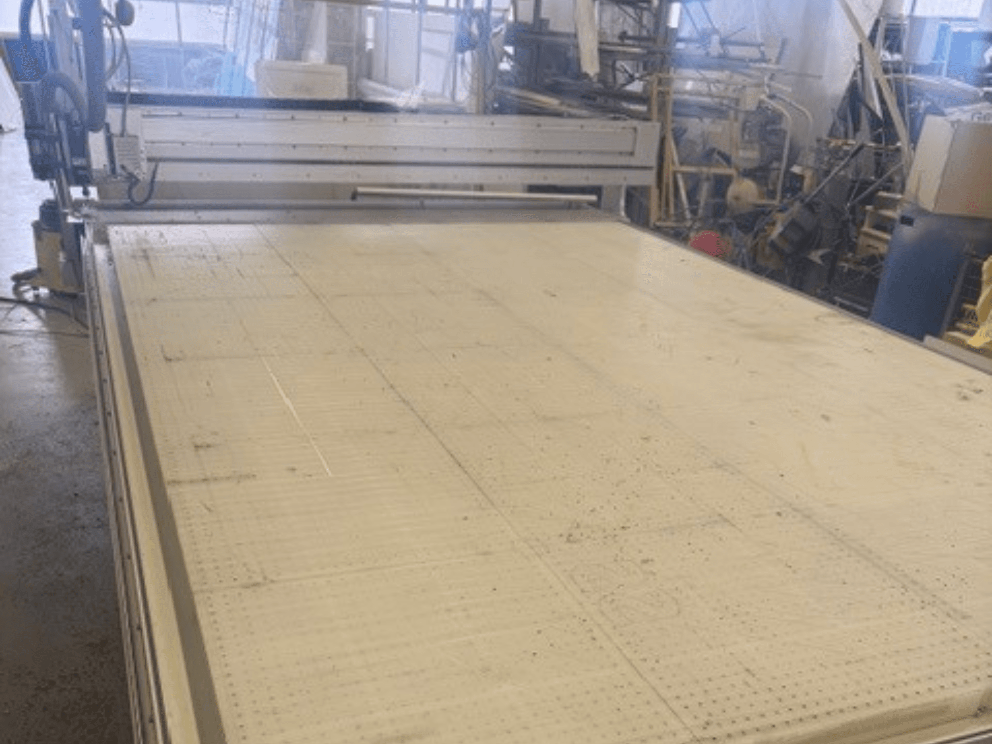 Liela griešanas iekārta ar līdzenu virsmu, redzams rāmis un vadotnes; skatīts no leņķa darbnīcā.