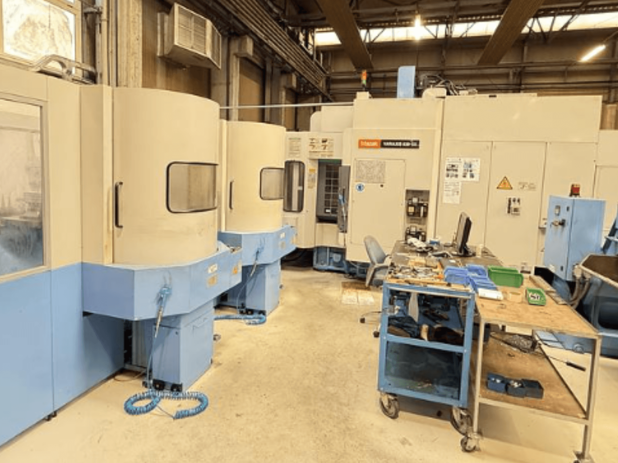 Mazak Variaxis 630-5X vertikālais apstrādes centrs darbnīcā, priekšējais skats, kurā redzams vadības panelis un instrumentu glabāšanas zona.