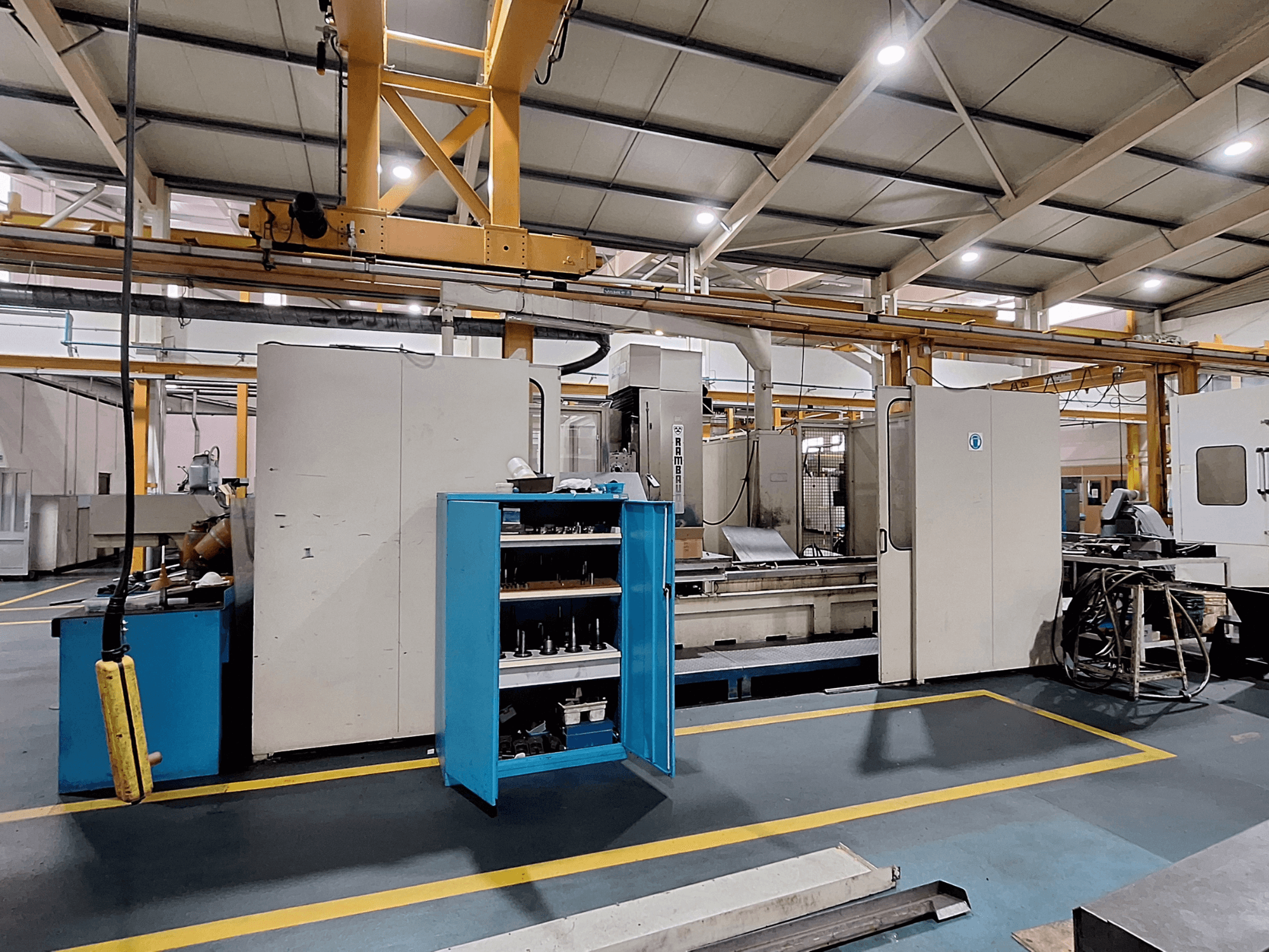 Portālfrēzmašīna Rambaudi RX 1250, skats no priekšpuses ar instrumentu glabāšanas vietu, plašā rūpnieciskā darba telpā.