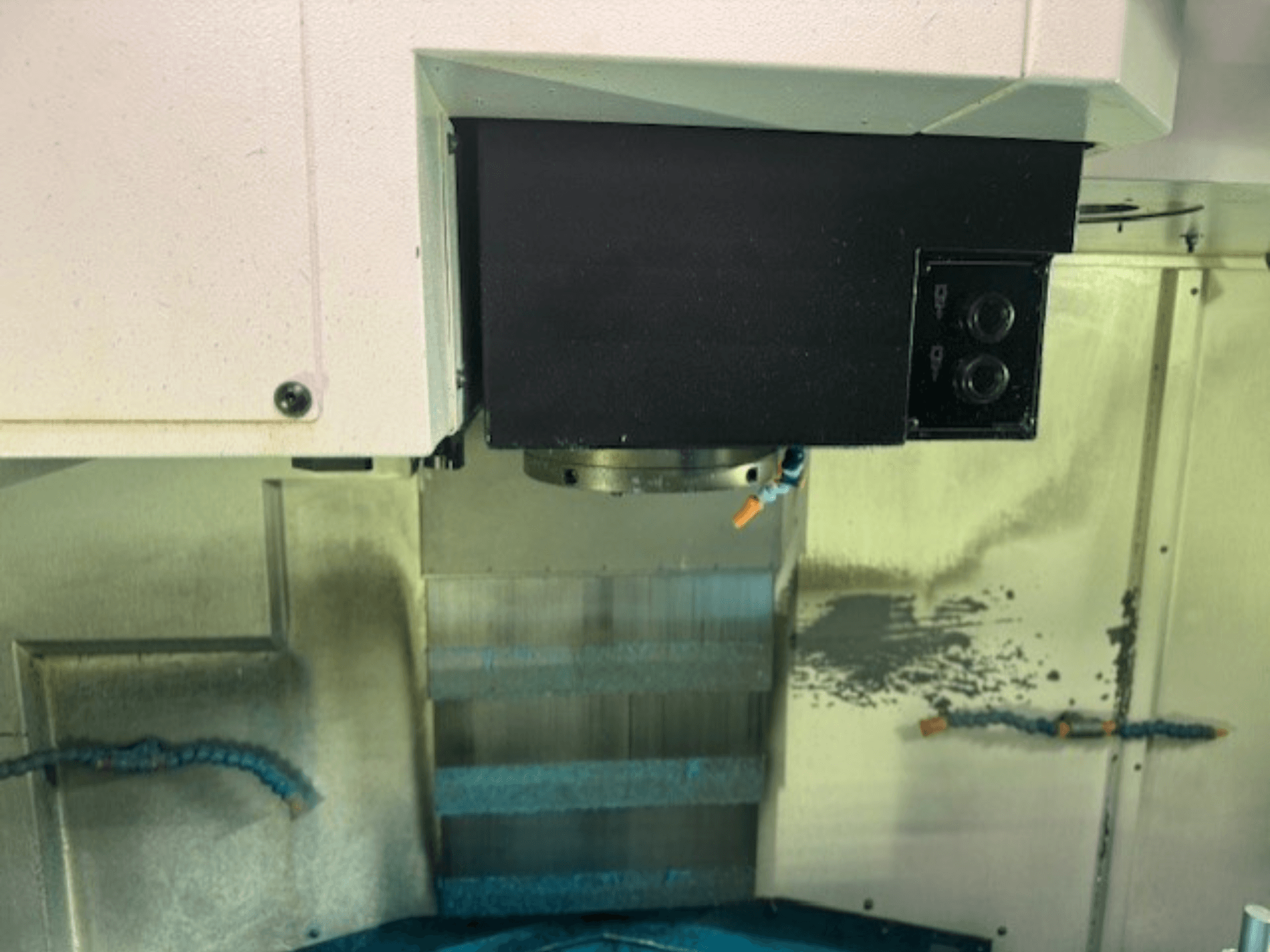 CNC frēzmašīnas vadības paneļa un instrumentu turētāja tuvplāns, kurā redzamas zīmola detaļas, pogas un darba virsma.