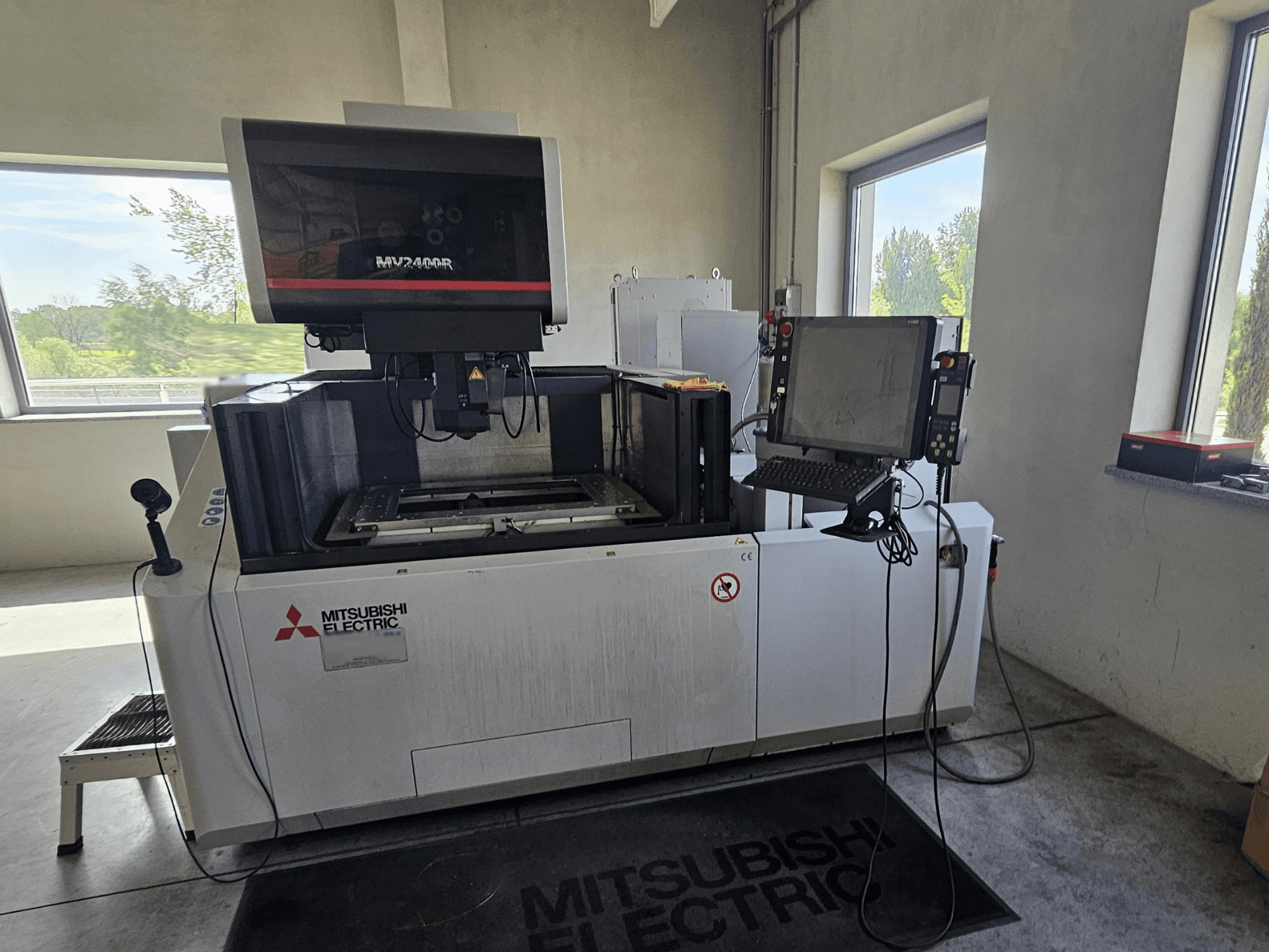 Mitsubishi MV2400R stiepļu EDM mašīna darbnīcā ar skārienjūtīgā ekrāna vadības paneli un darba zonas laukumu.