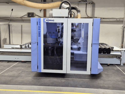 HOMAG BMG 512 ProfiLine CNC mašīna, skats no priekšpuses, ar stikla paneli, redzamiem precīziem instrumentiem un rūpniecisku iestatījumu.