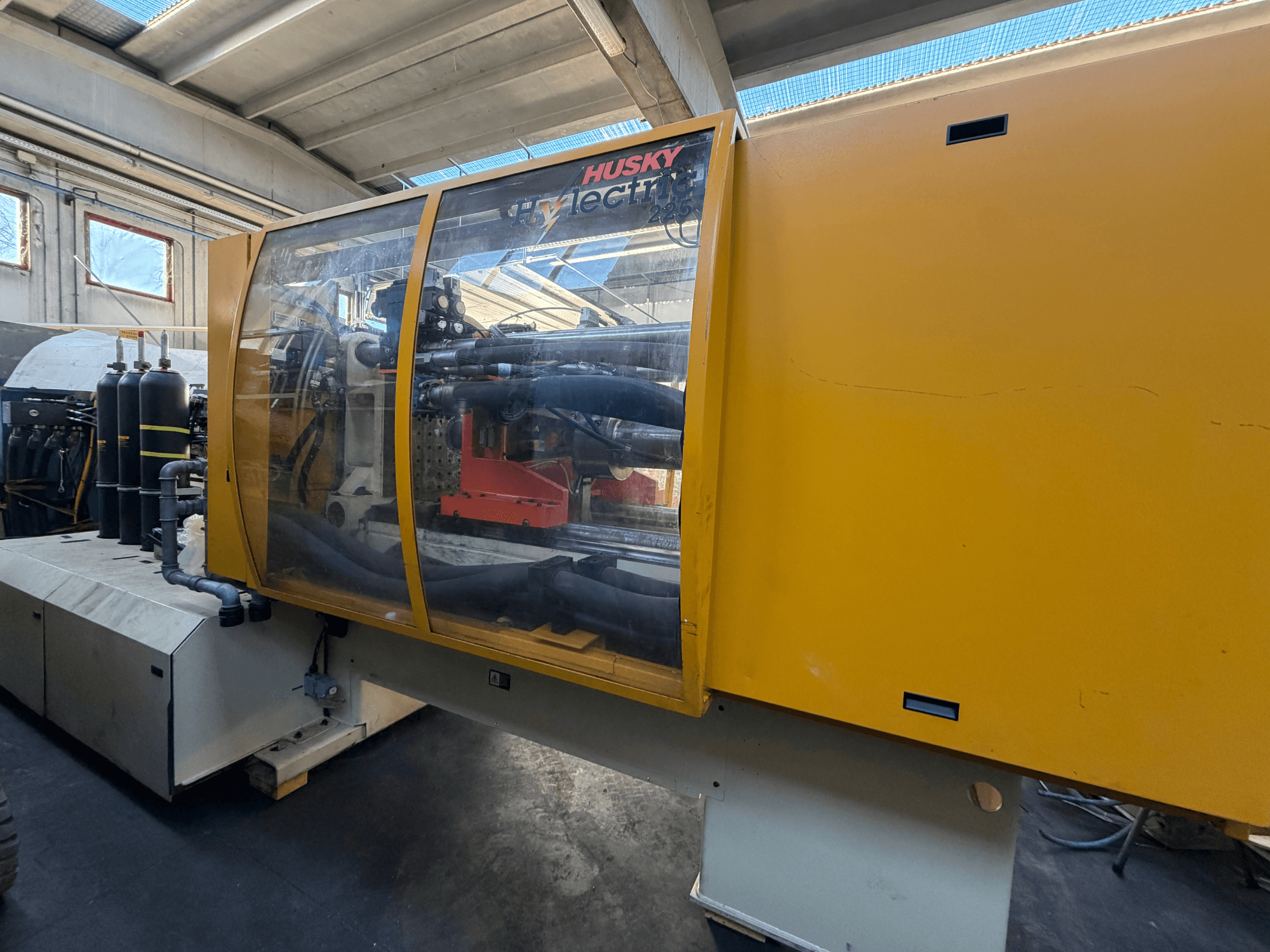 Husky HL225 RS65 elektriskā iesmidzināšanas iekārta, priekšējais skats ar dzeltenu korpusu, redzamo vadības paneli un hidrauliskajiem komponentiem.