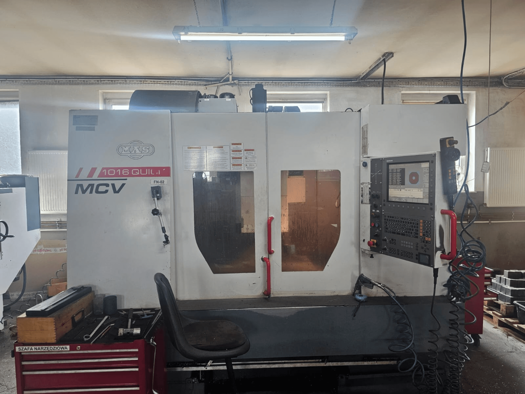 MVS MCV 1016 QUILL CNC darbgalds, skats no priekšpuses, ar vadības paneli, instrumentu atvilktni un darba vietu ar instrumentiem.