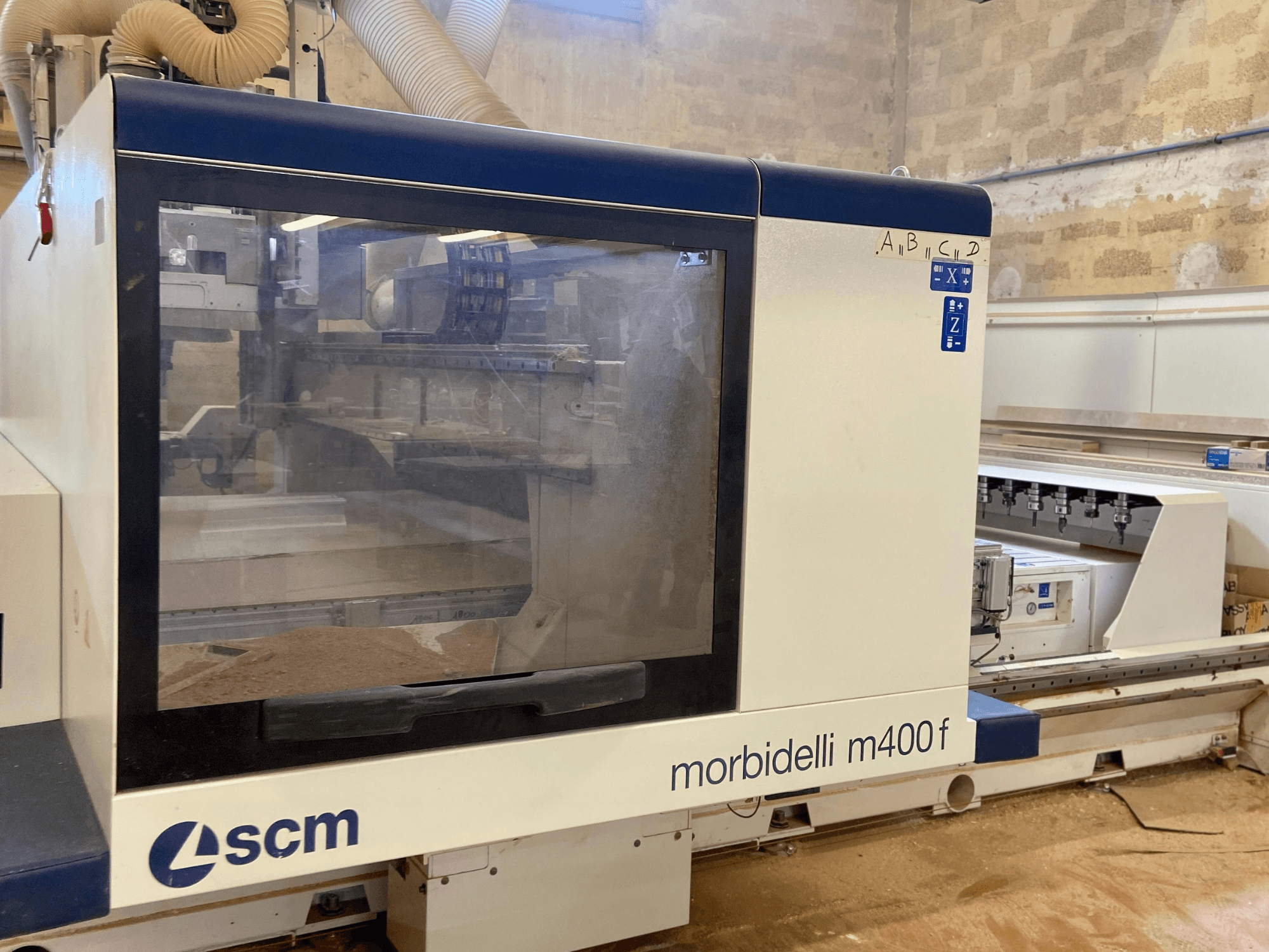 SCM Morbidelli M400F CNC mašīna, skats no priekšpuses, ar vadības paneli un redzamām zāģu skaidām uz grīdas.