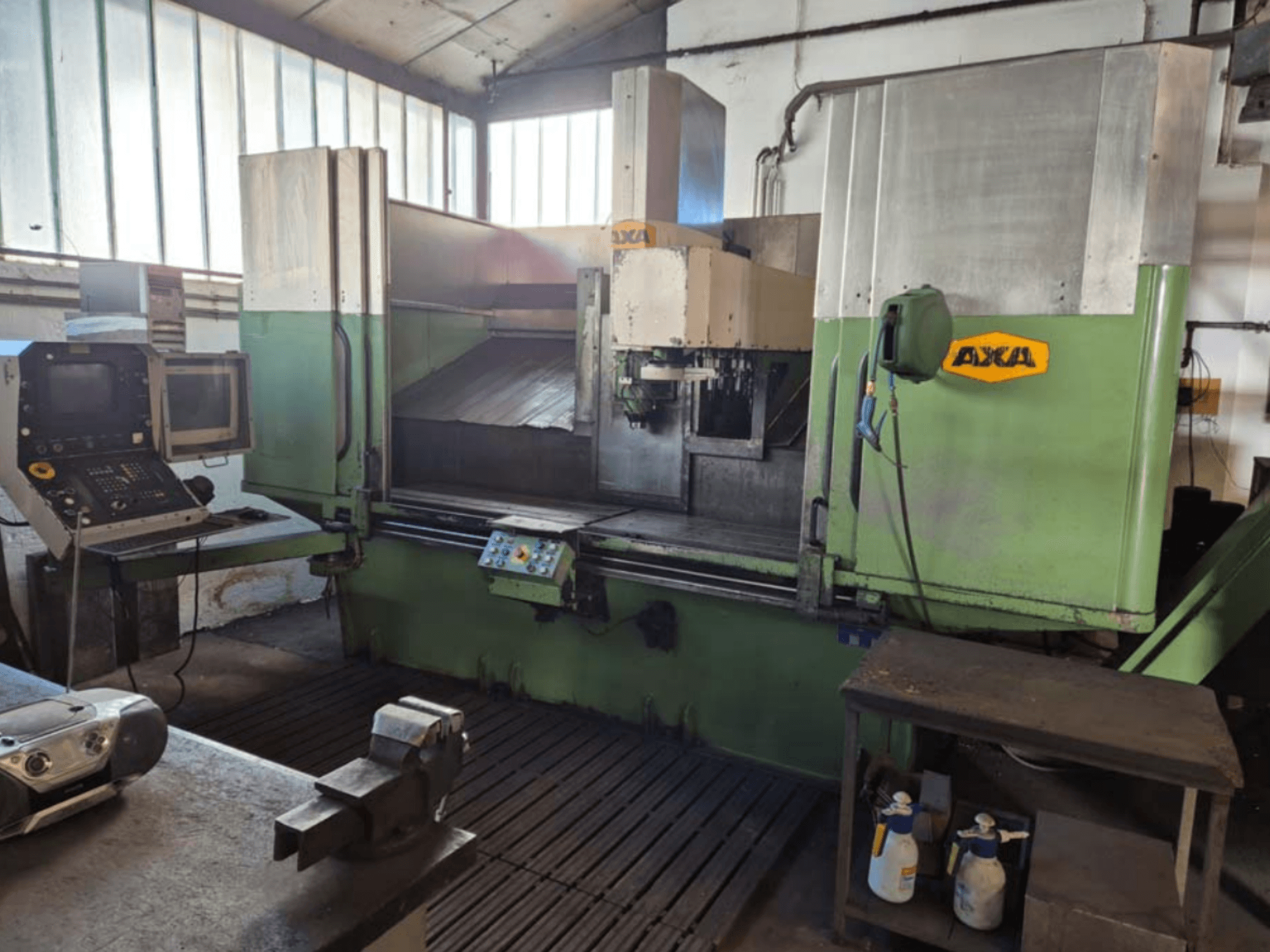 AXA VSC-2M vertikālais apstrādes centrs, skats no priekšpuses, ar vadības paneli un darba zonu ar griezējinstrumentiem un tīrīšanas piederumiem.