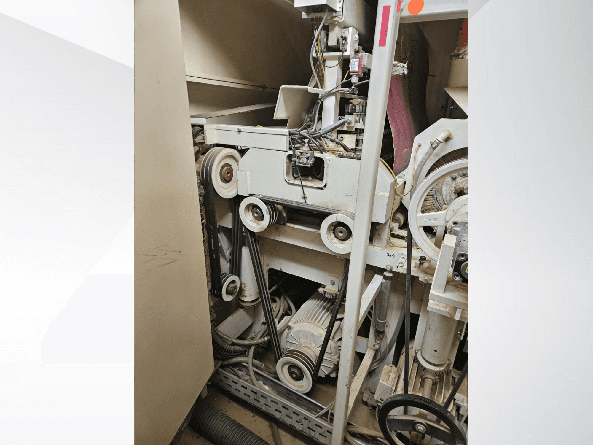 Rūpnieciskās mašīnas iekšpuse ar siksnām un skriemeļiem, ar motoru un elektroinstalāciju, skatīts no sāniem.