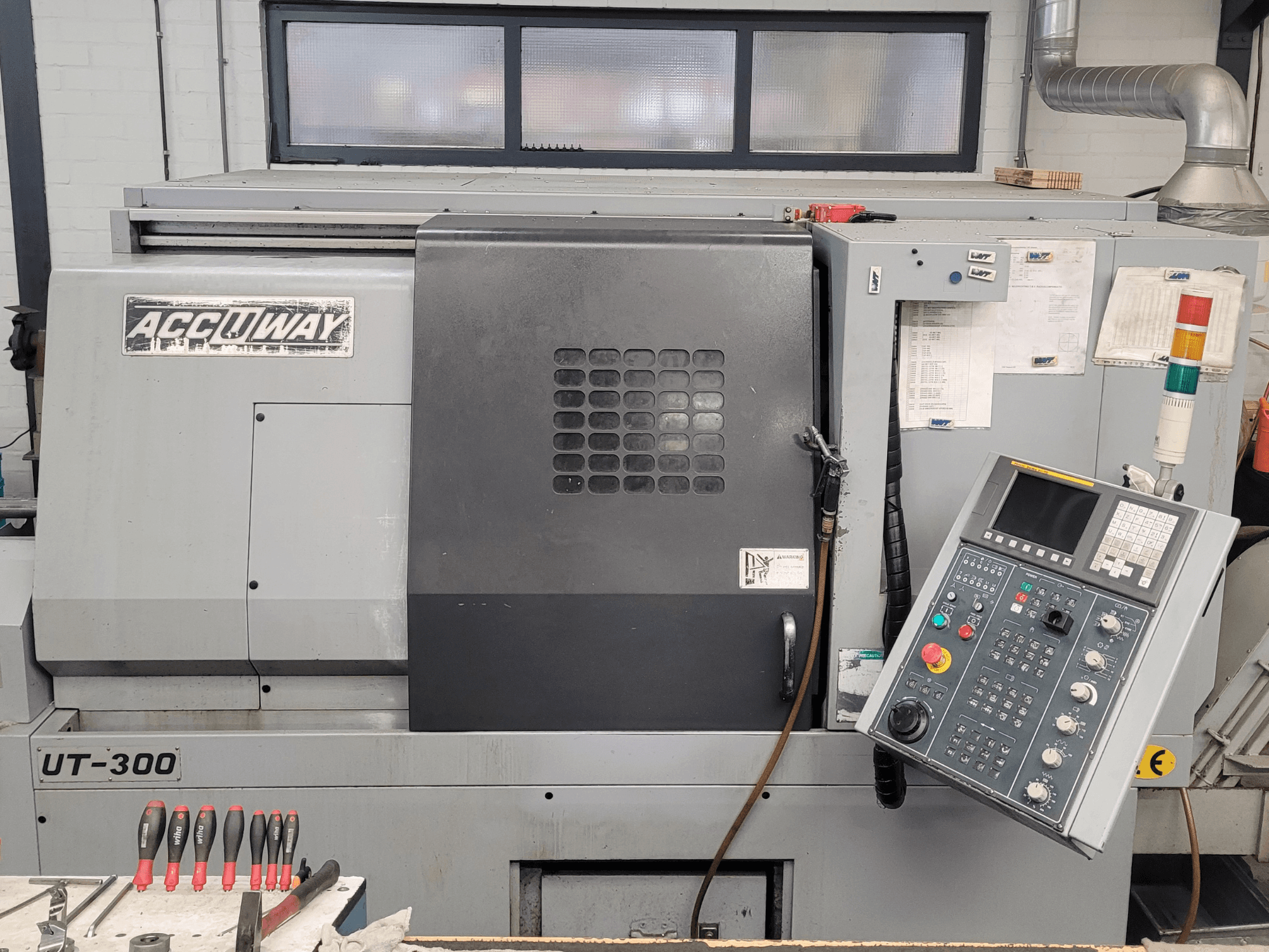 Accuway UT-300 CNC mašīna priekšpusē ar vadības paneli un dažādām vadības pogām darbnīcā.