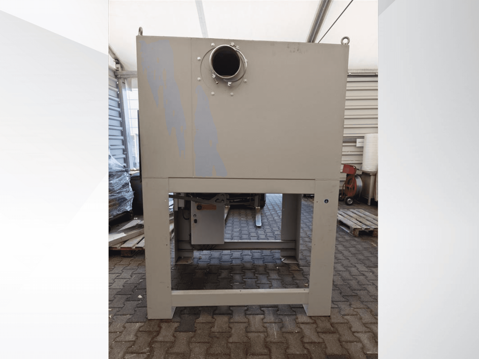 Pelēks rūpnieciskais putekļu savācējs no priekšpuses, ar lielu apaļu atvērumu un uzstādīts uz izturīgas pamatnes.