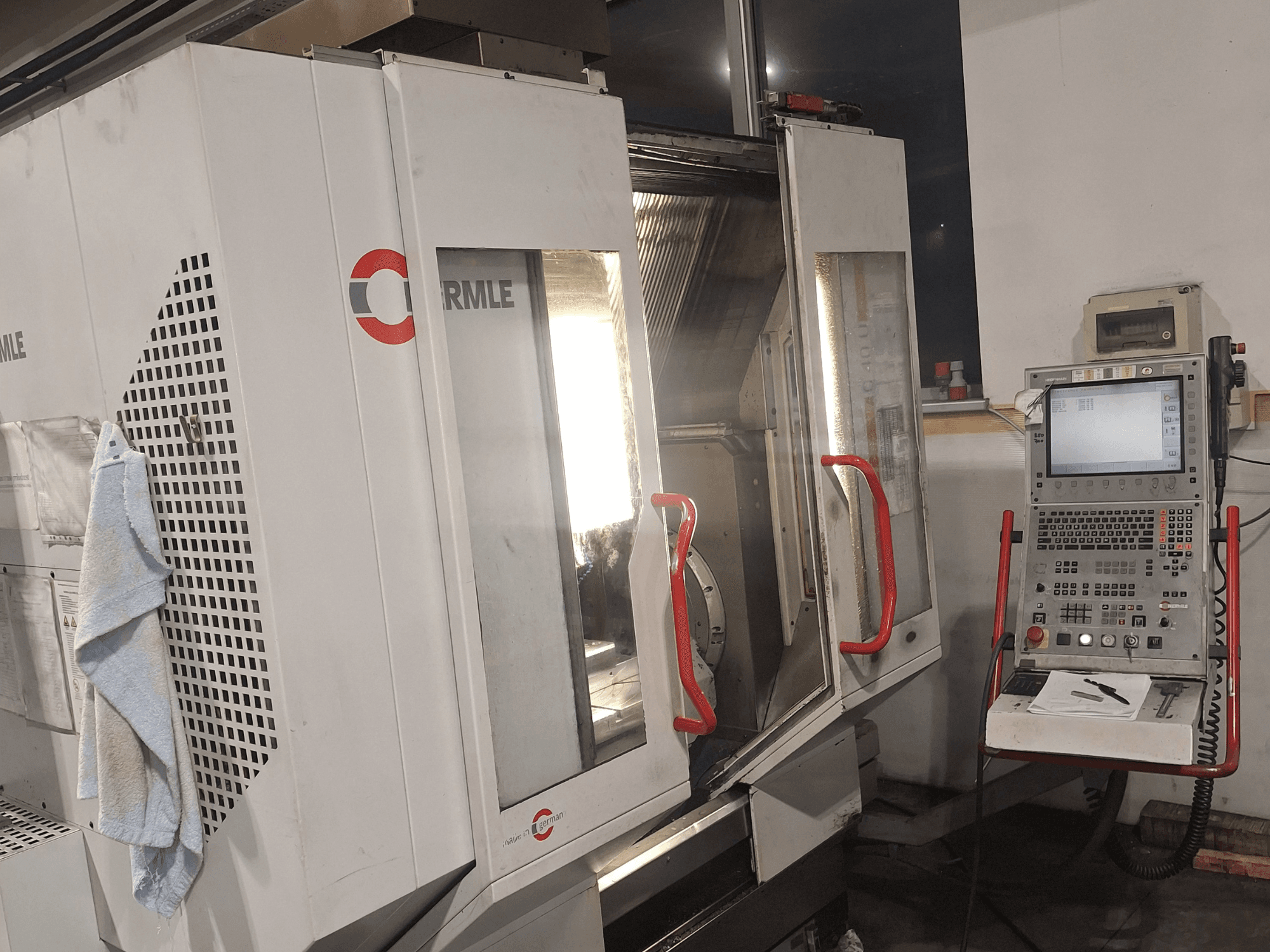 Cormile zīmola CNC mašīna, priekšējais skats, kurā redzamas daļēji atvērtas durvis un vadības panelis ar ekrānu un pogām.