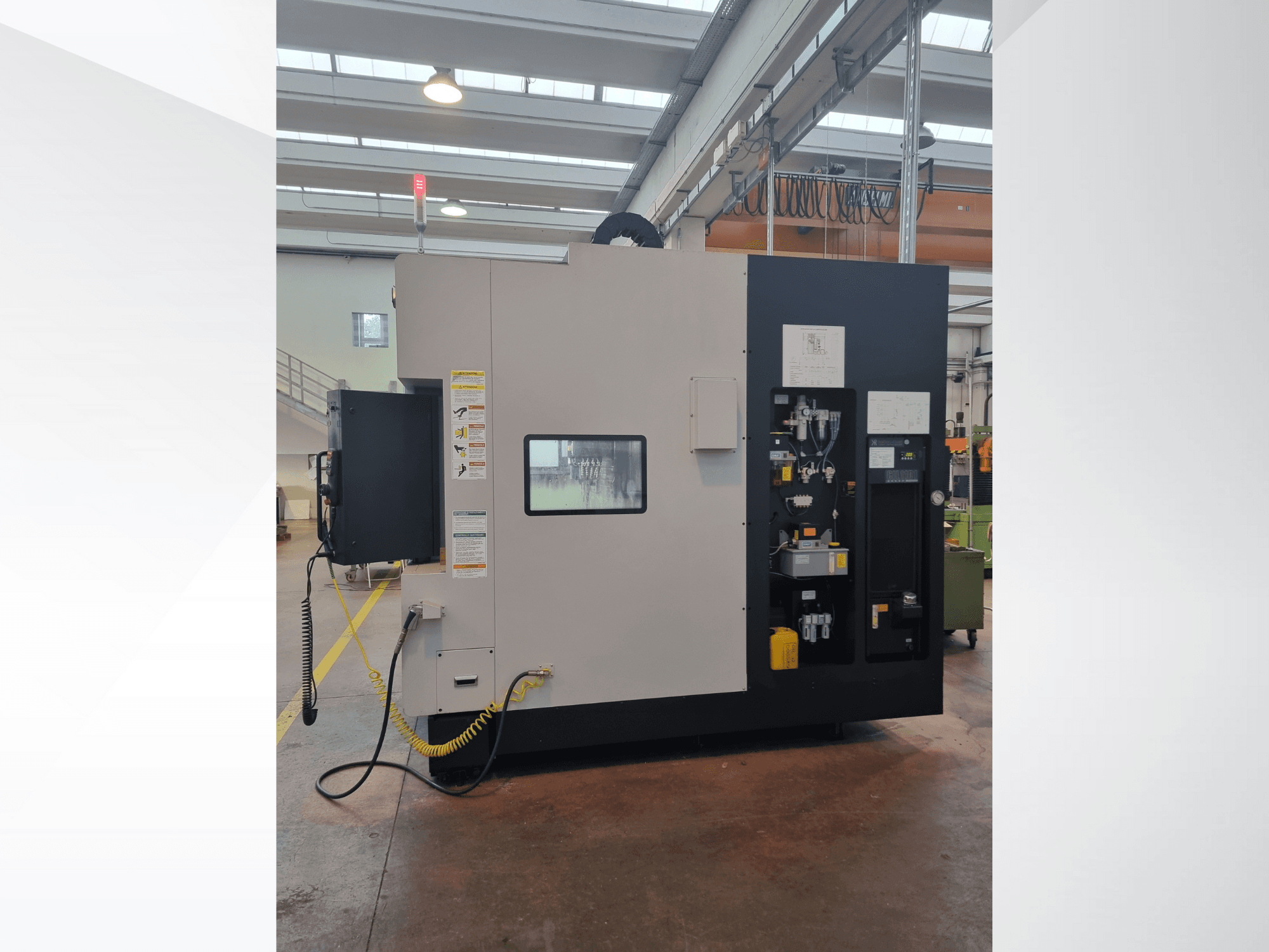 Rūpnieciskajai mašīnai no sānu skata ir vadības panelis ar pogām, indikatoriem un drošības brīdinājuma uzlīmi.