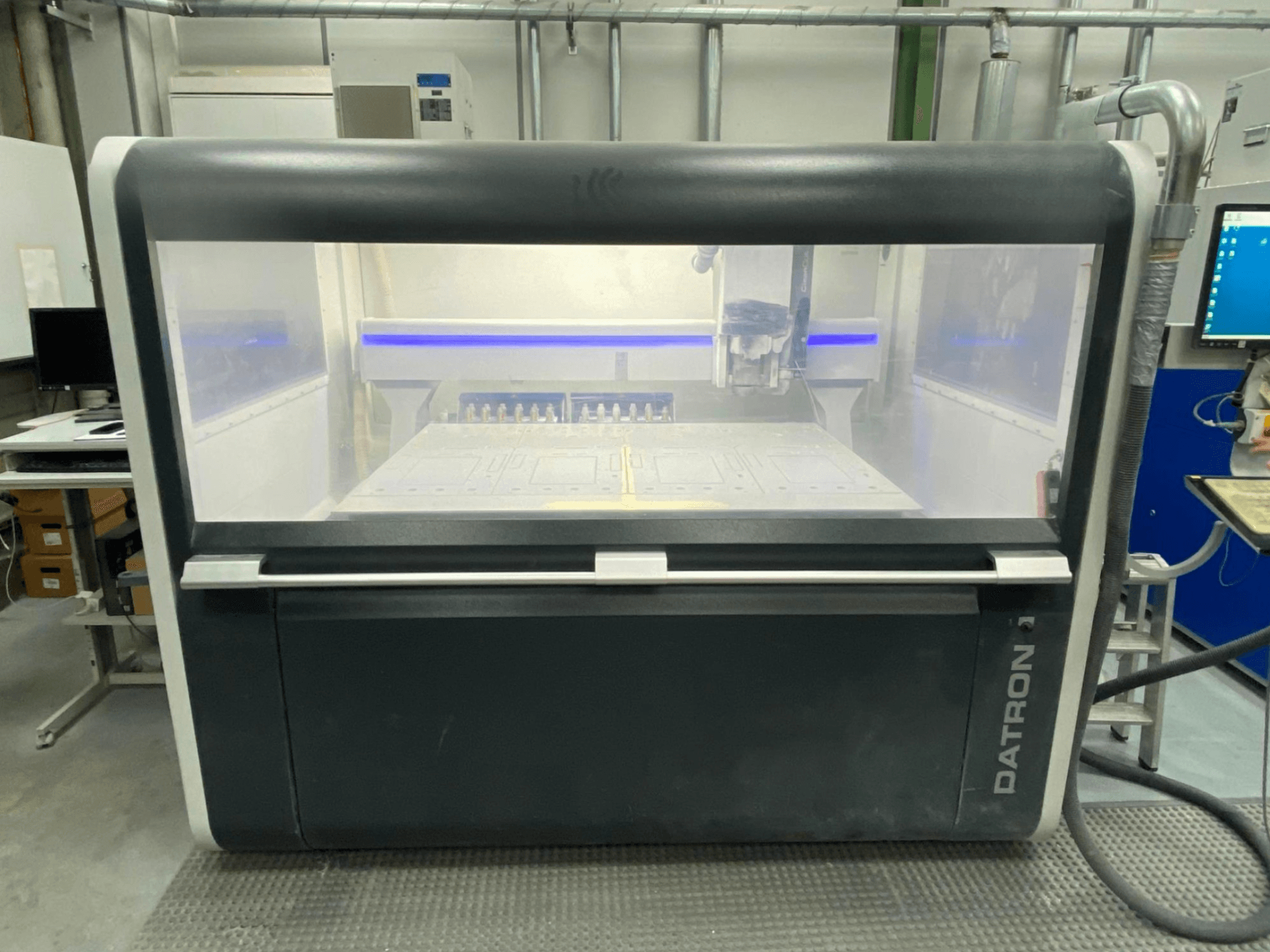 Datron MLCube B vertikālā apstrādes centra priekšējais skats, kurā redzams caurspīdīgais korpuss un vadības panelis.