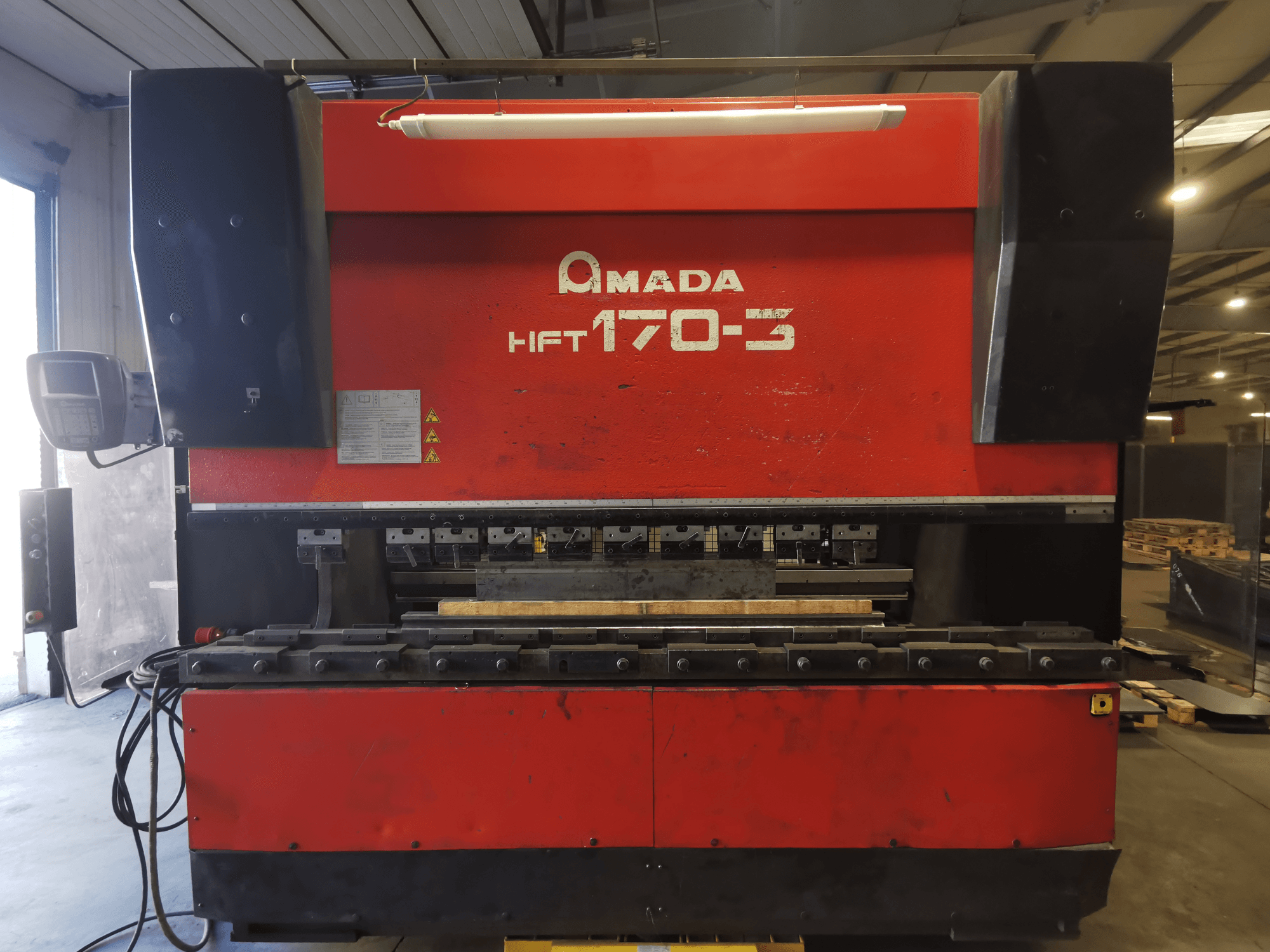 Sarkanā Amada HFT 170-3 preses bremze no priekšpuses, redzams vadības panelis, lieces instrumenti un darba virsma.