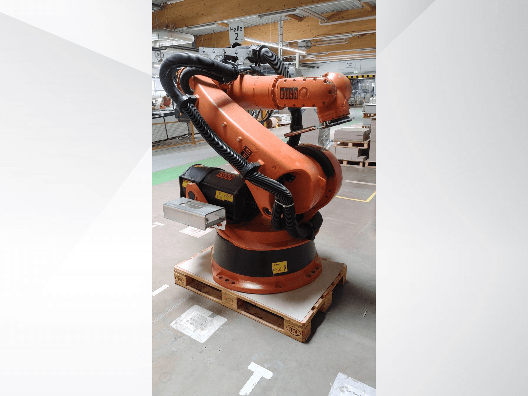 KUKA KR140-3 COMP robota roka oranžā krāsā, priekšējais skats uz koka paliktņa, ar izliektu roku un vadības bloku.