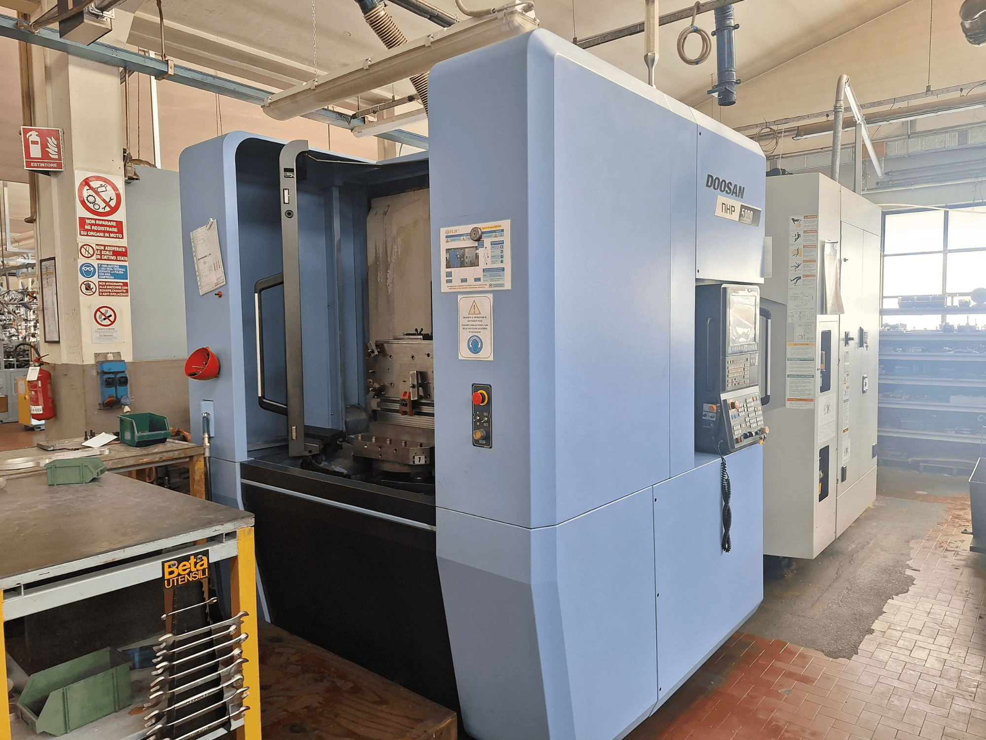 DOOSAN NHP 5000 horizontālais apstrādes centrs darbnīcā, sānu skats, kurā redzams tā vadības panelis un apstrādes zona.
