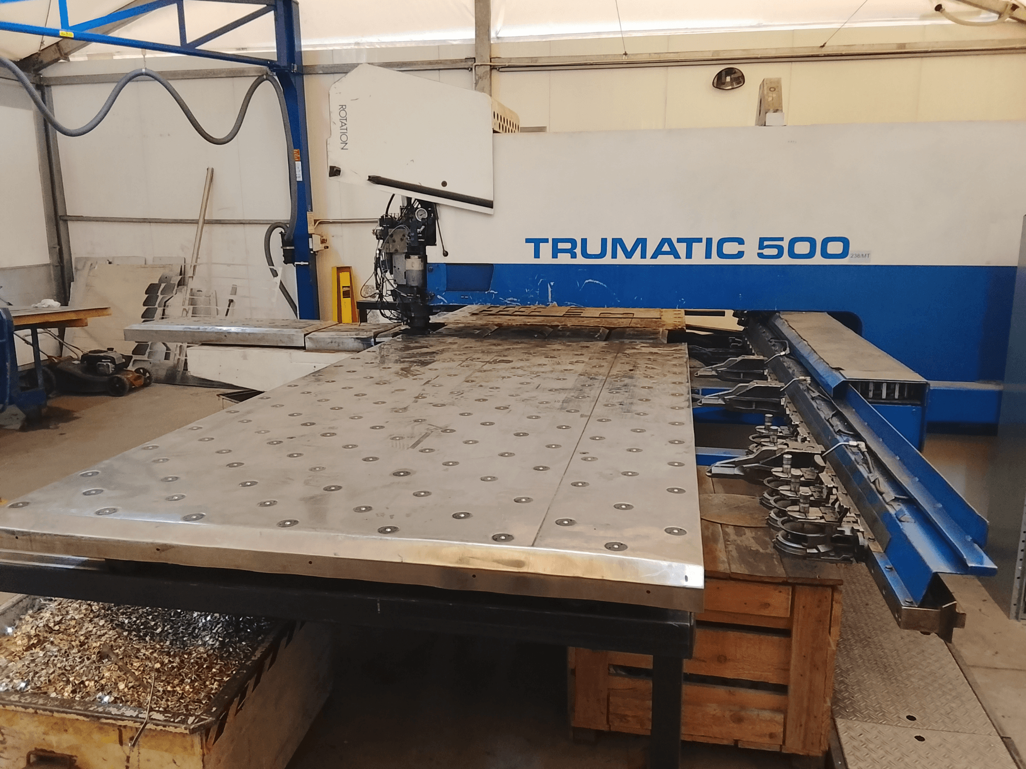 Trumatic 500 CNC darbgalds, skats no augšas, ar lielu metāla griešanas galdu, zem kura ir uzstādīti instrumenti un skaidas.