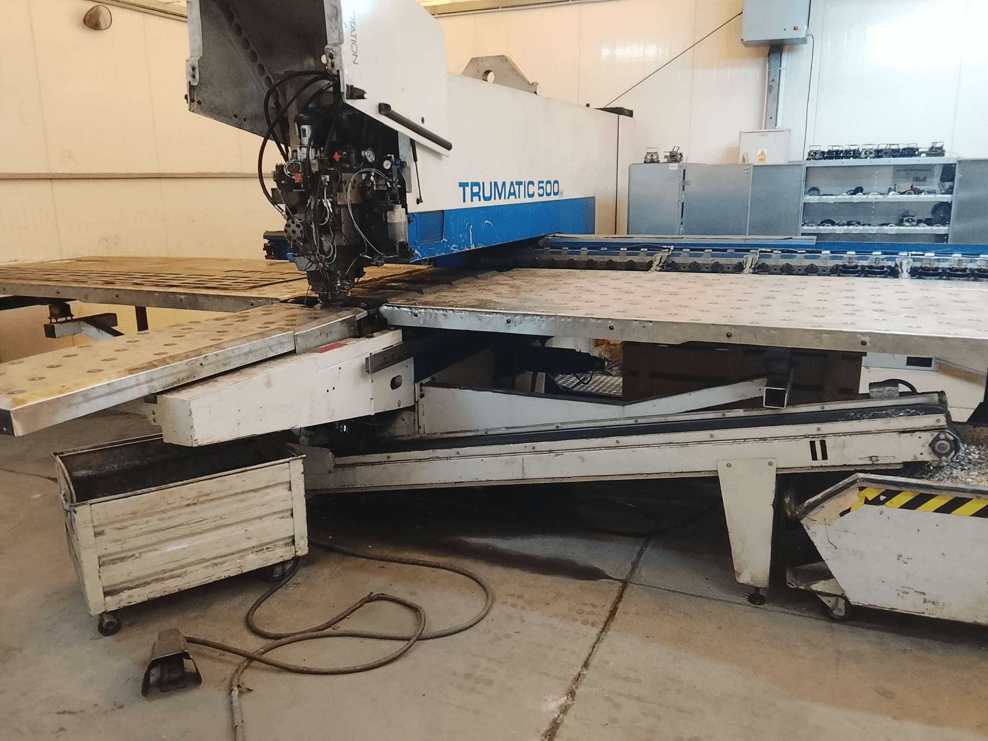 TRUMATIC 500 CNC darbnīcā, skats no sāniem, kurā redzama griešanas galva un metāla darbagalds ar iepriekš izurbtiem caurumiem.