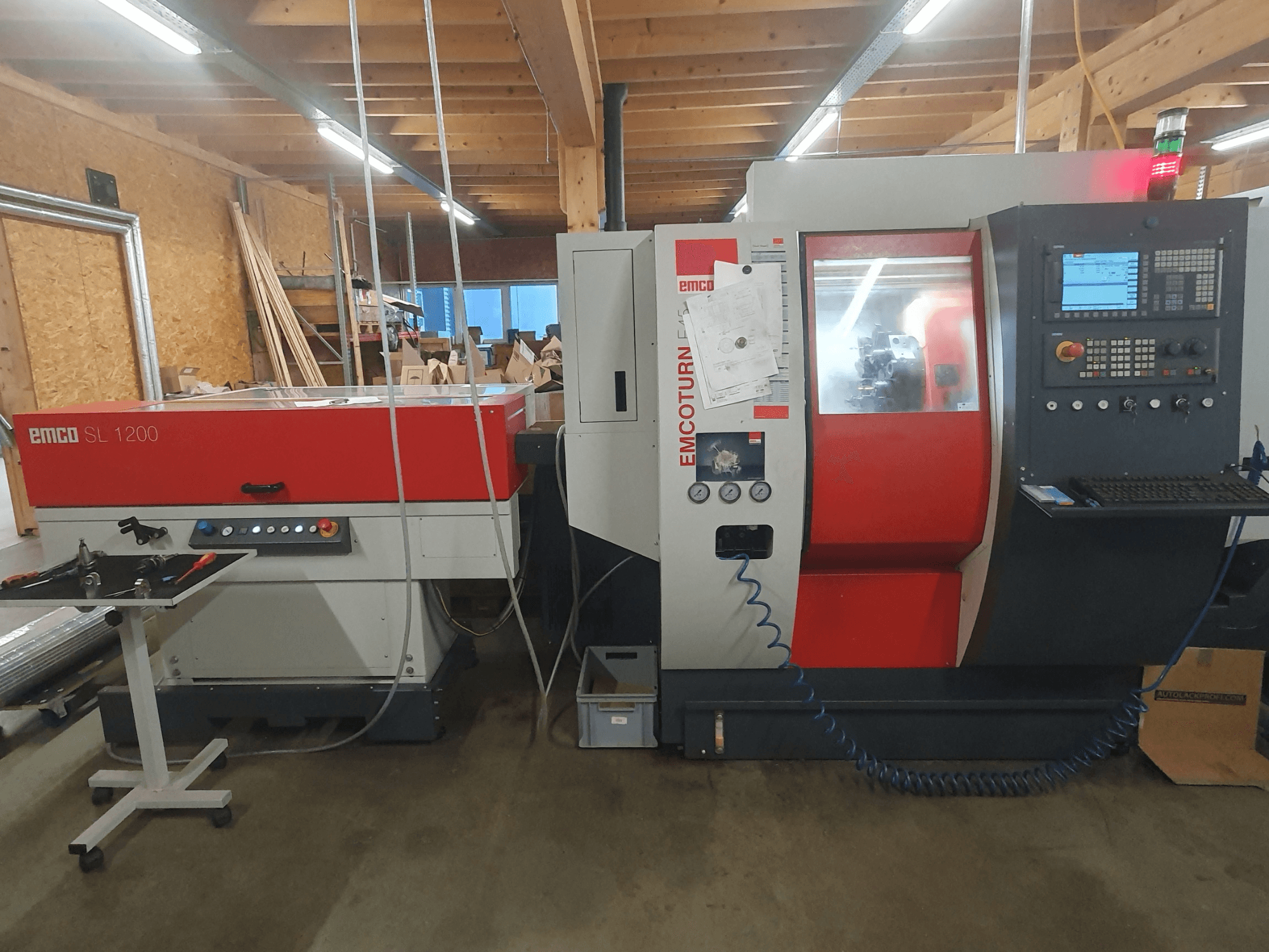 EMCO SL 1200 CNC virpa un EMCOturn; priekšējais skats, kurā redzamas vadības ierīces, displeji un darbības indikatori darbnīcā.