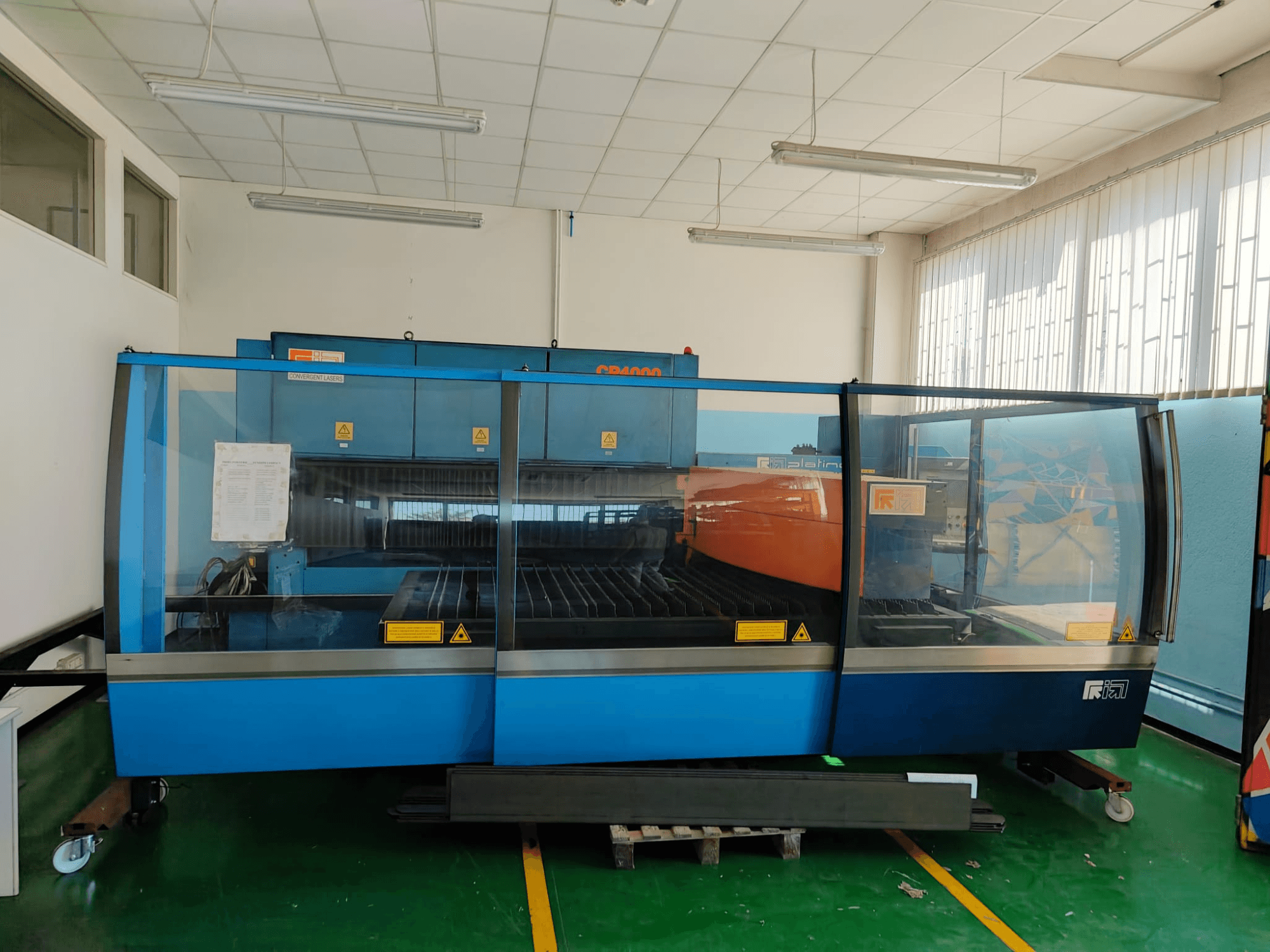 CONVERGENT LASERS CP4000 CO₂ lāzergriešanas iekārtas priekšskats ar zilu un oranžu dizainu labi apgaismotā darbnīcas vidē.