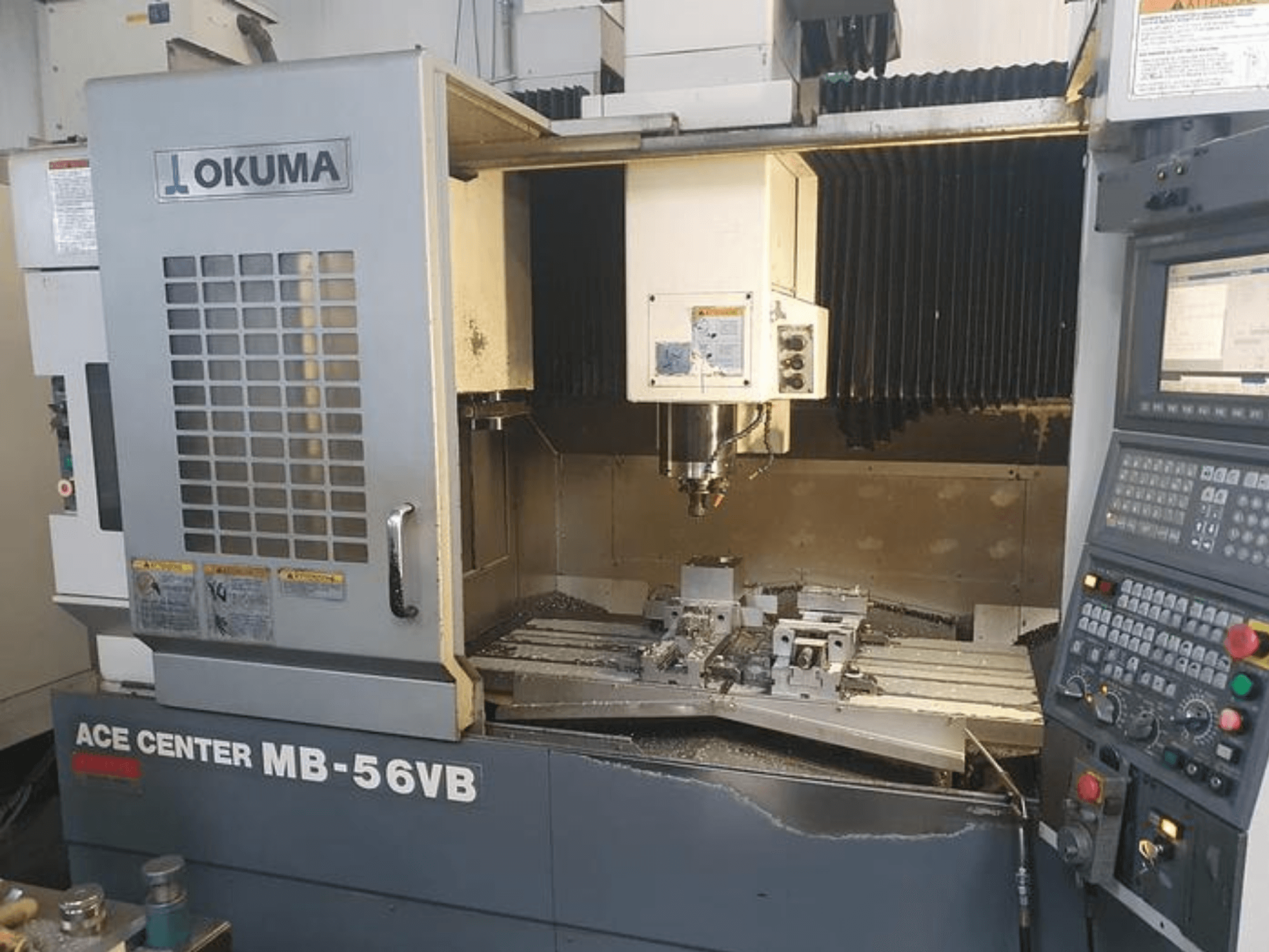 Okuma ACE CENTER MB-56VB CNC frēzmašīna priekšpusē, kurā redzams vadības panelis un apstrādes zona.