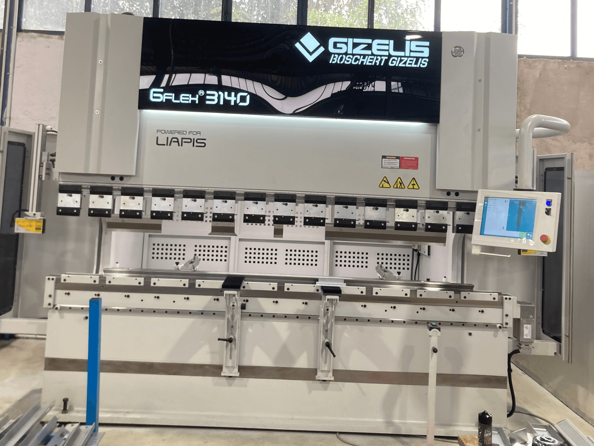 Hidrauliskā prese GIZELIS G-FLEX 3140 priekšpusē ar vadības ekrānu, ar vairākiem lieces instrumentiem un drošības marķējumiem.