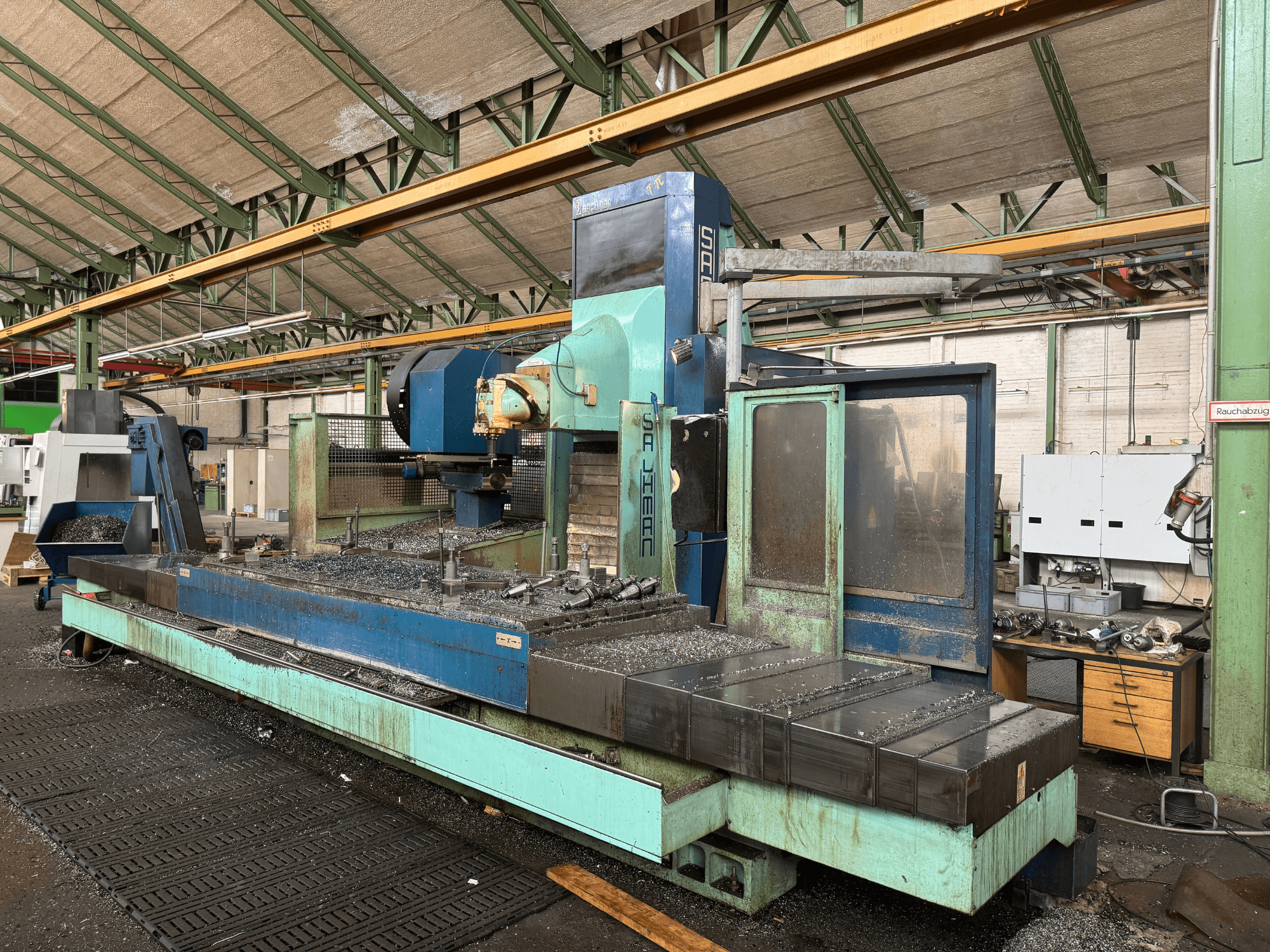 Salvador frēzmašīna rūpnīcā, skats no priekšpuses, zilā un zaļā krāsā, uz gultas redzamas metāla skaidas.