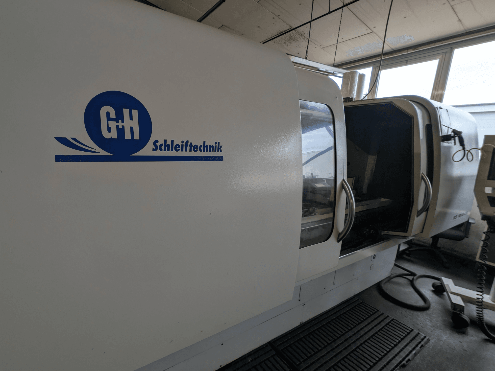 Cilindriskās slīpmašīnas GEIBEL & HOTZ RS 1000 CU, sānu skats, kurā redzams vadības panelis un atvērtas piekļuves durvis.