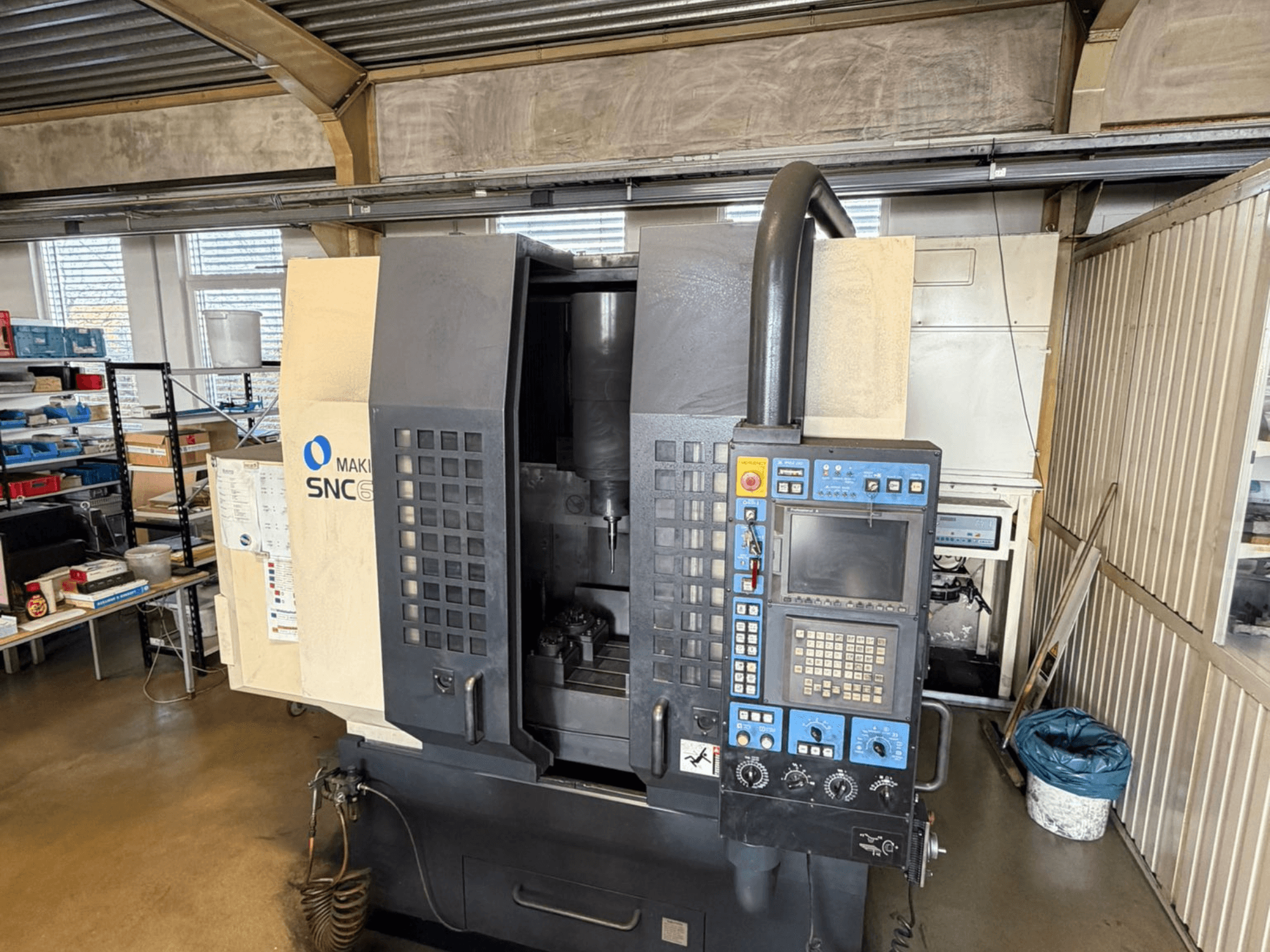 Makino SNC 64-A15 vertikālais apstrādes centrs priekšpusē, kurā redzams vadības panelis, apstrādes zona un rūpnieciskā darba telpa.