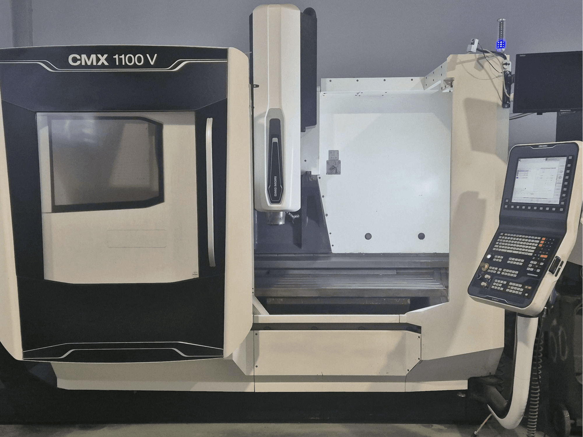 Vertikālais apstrādes centrs DMG MORI CMX 1100 V, skats no priekšpuses, kurā redzams vadības panelis un mašīnas galds.