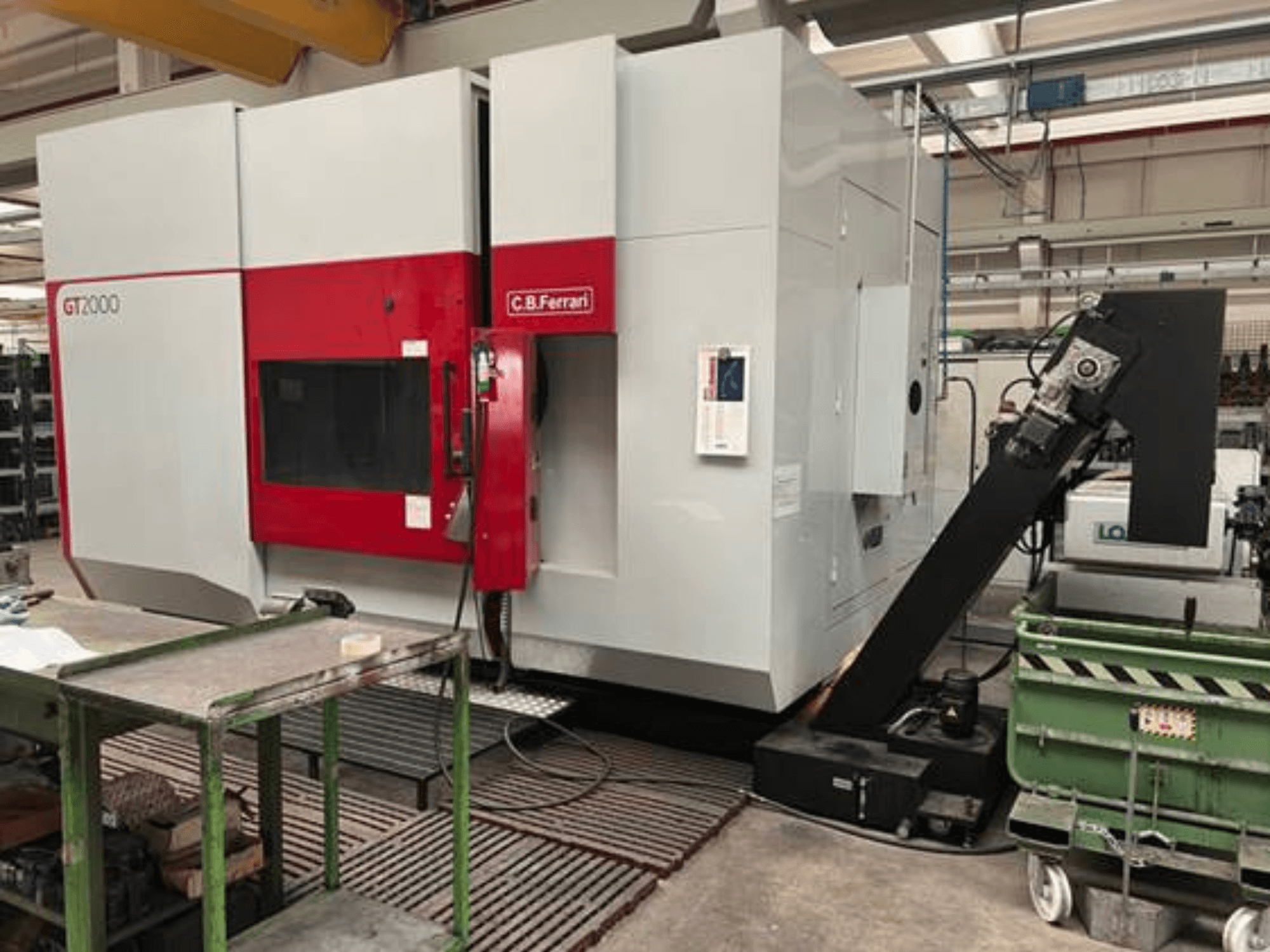 C.B. Ferrari GT2000 frēzmašīna priekšpusē ar robotizētu roku un rūpniecisku darba vietu ar zaļo ratiņu.