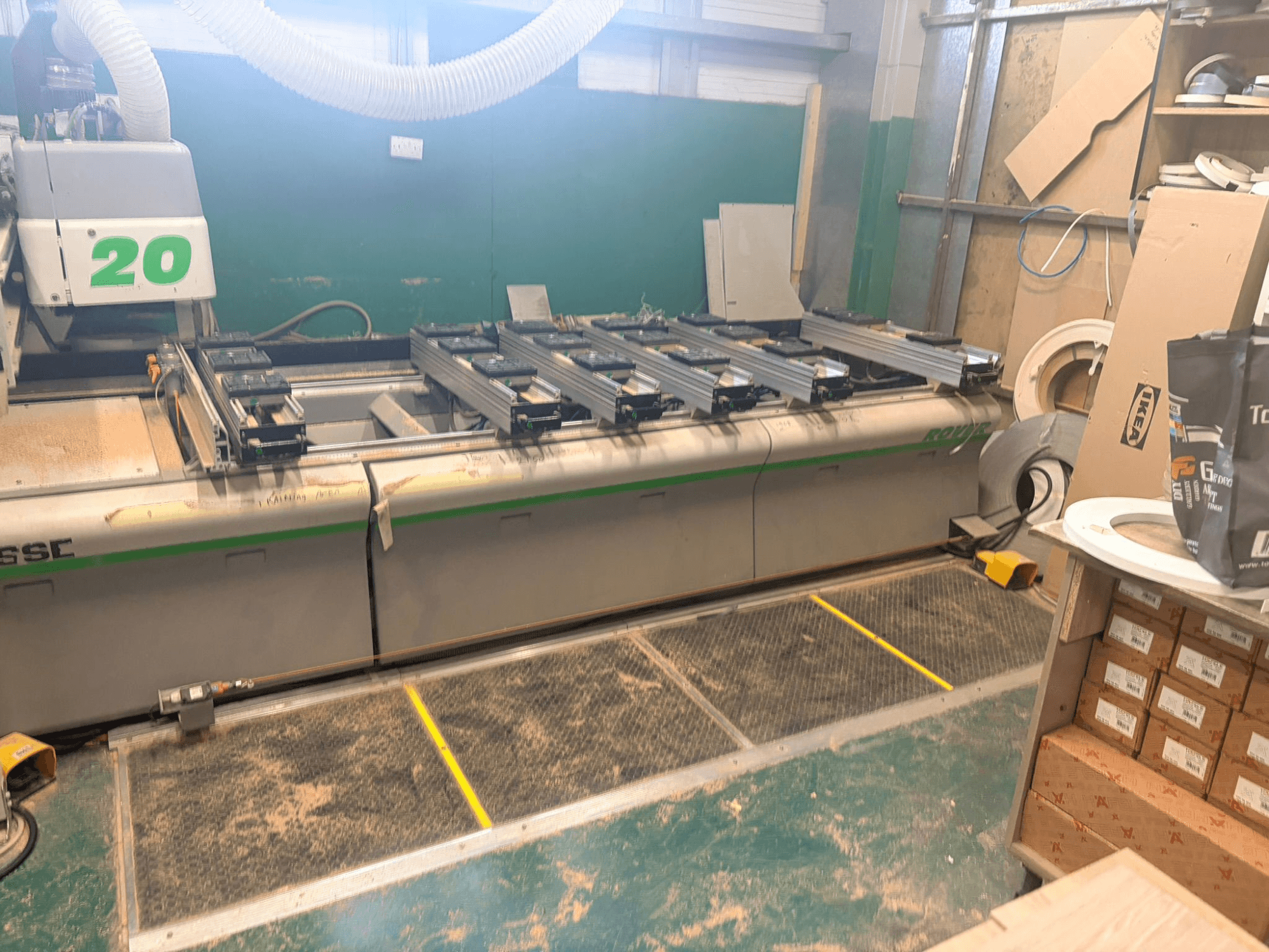 CNC kokapstrādes centrs BIESSE ROVER 20, skats no priekšpuses, ar sliedes sistēmu, vadības ierīcēm un uz virsmas redzamām zāģu skaidām.