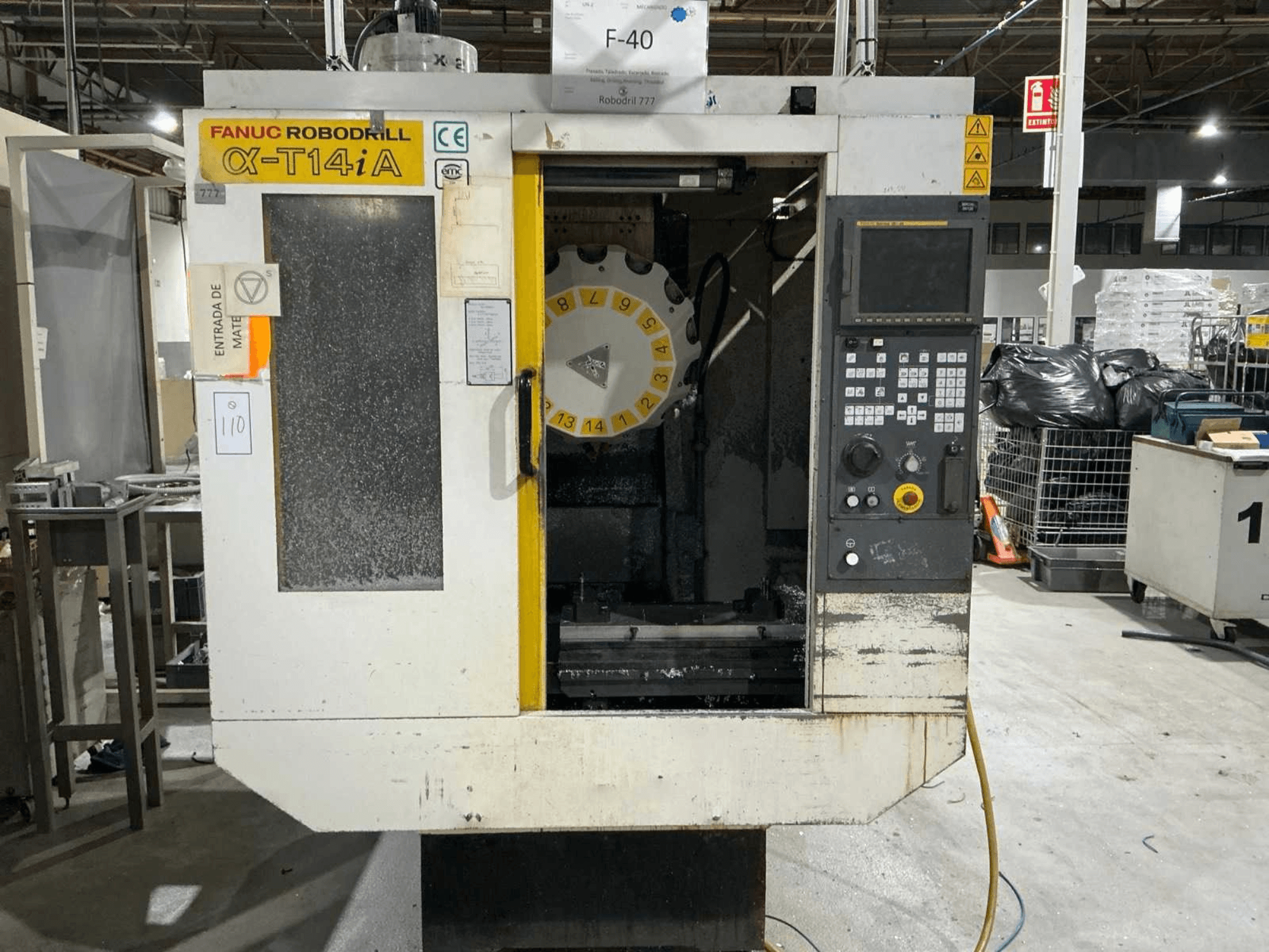 FANUC ROBODRILL α-T14iB vertikālais apstrādes centrs, priekšējais skats, kurā redzams vadības panelis un instrumentu karuselis.