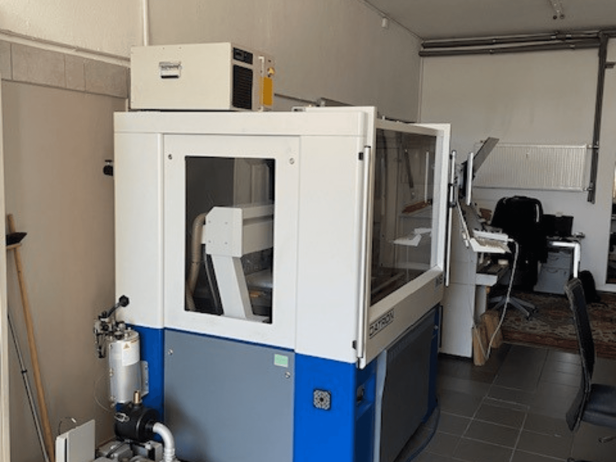 Zilā un baltā rūpnieciskā iekārta ar caurspīdīgiem paneļiem, skats no priekšpuses, ietver vadības piekļuvi un redzamu ventilācijas bloku.
