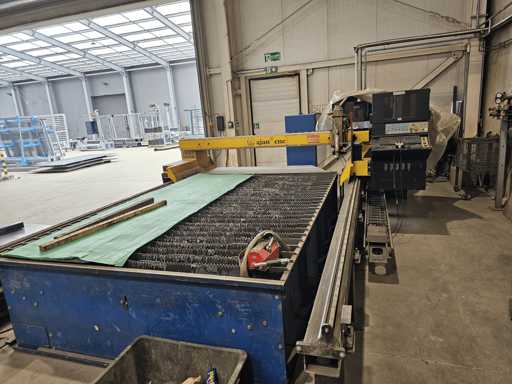 AJAN PP16011 Automātiskā plazmas griešanas iekārta ar griešanas galdu un vadības paneli darbnīcas vidē.