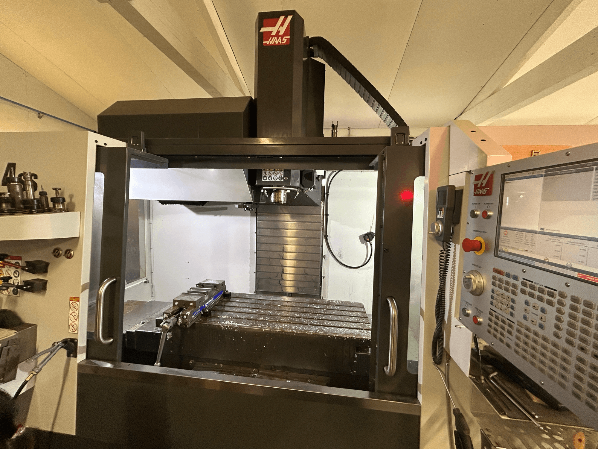 HAAS VF-4SS vertikālais apstrādes centrs, priekšējais skats, kurā redzams vadības panelis, instrumentu turētājs un darba zona ar metāla skaidām.