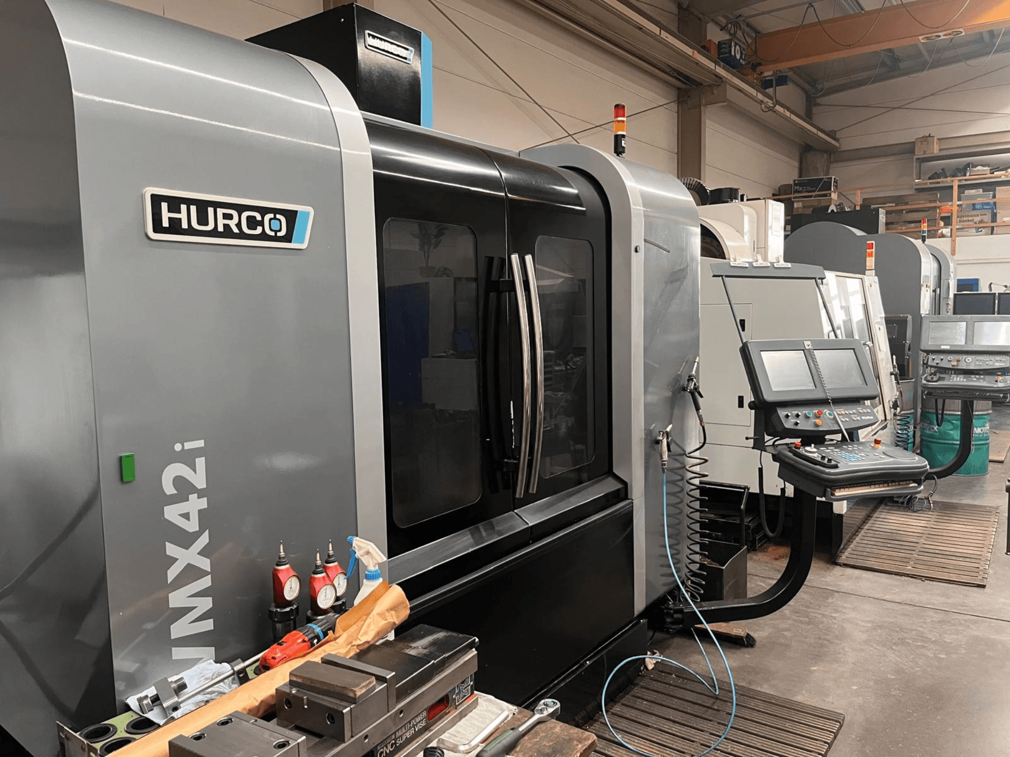 Hurco VMX42i CNC darbnīcā, skats no priekšpuses, ar vadības paneli un dažādiem instrumentiem uz darbgalda.