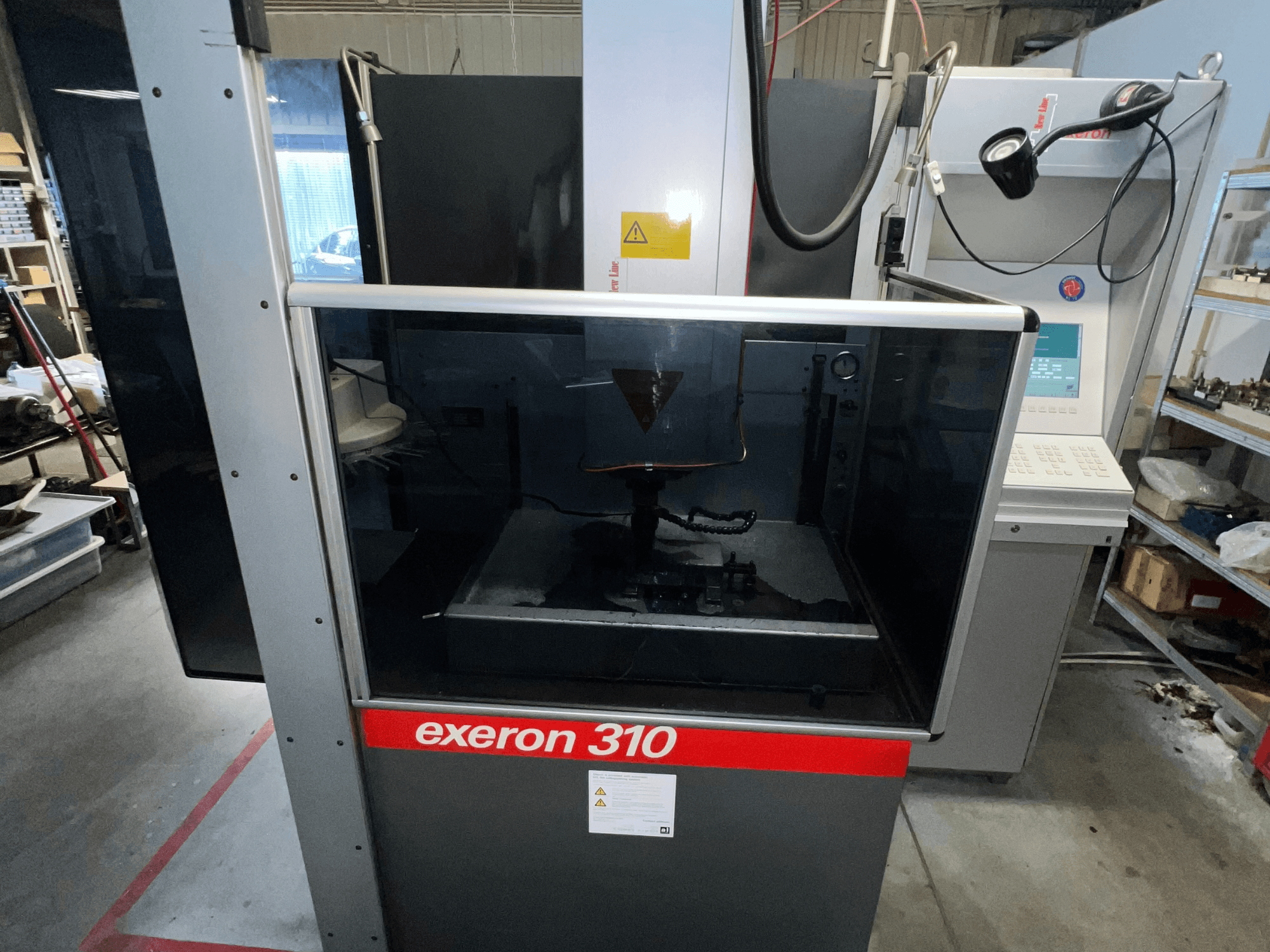 Exeron 310 mašīnas priekšējais skats, kurā redzama stikla kamera un vadības panelis līdzās darba vietas plauktiem.