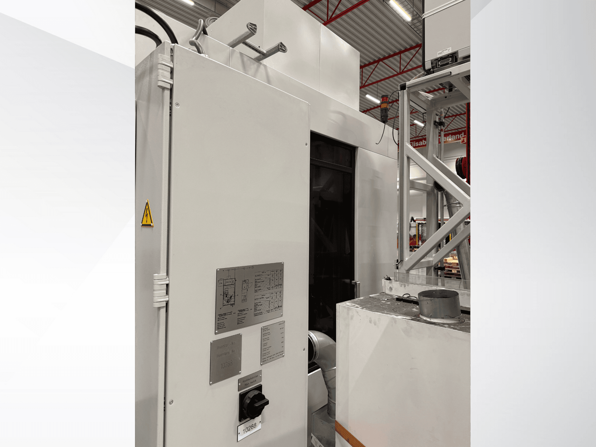 Skats no sāniem uz baltu rūpniecisku mašīnu ar vadības paneli un brīdinājuma uzlīmi, kas ir daļa no automatizētas sistēmas.