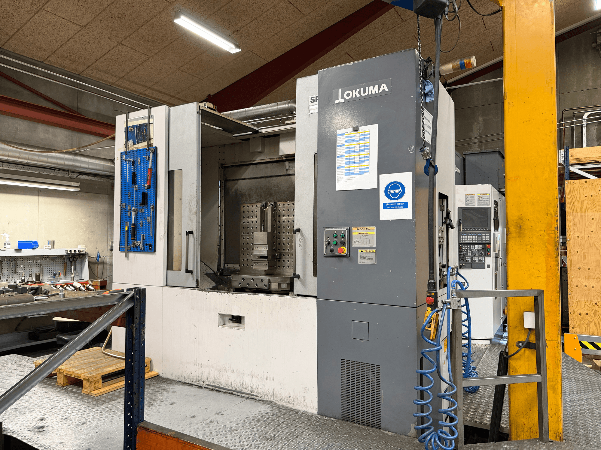 Okuma MA-600HB horizontālais apstrādes centrs darbnīcā — skats no priekšpuses, kurā redzams vadības panelis un darba zona.