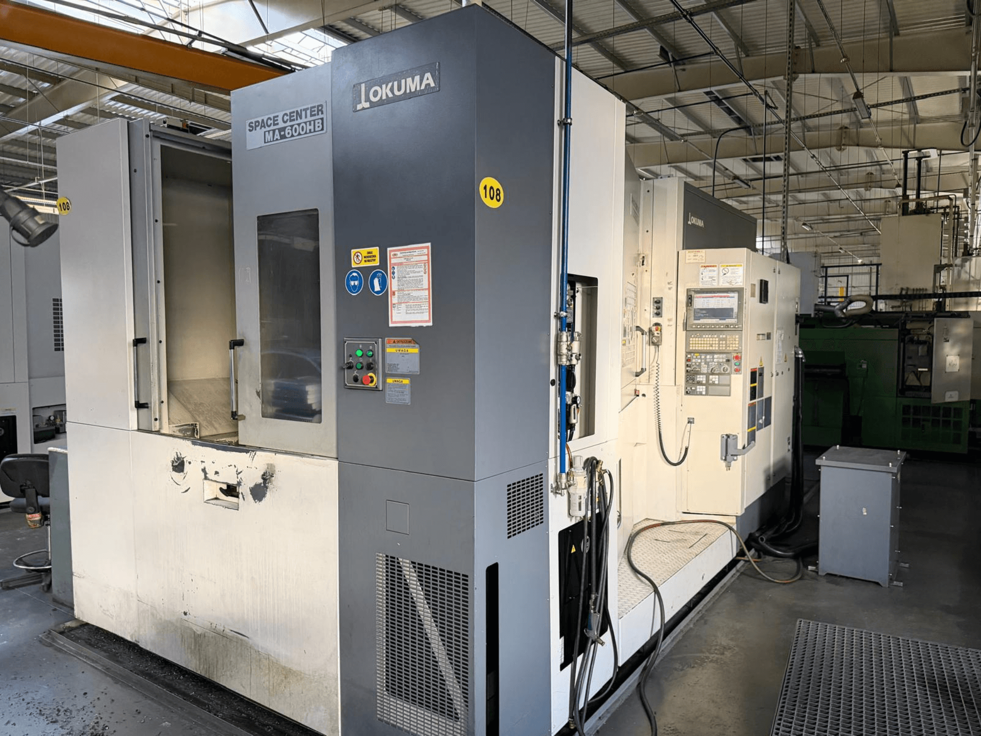 Okuma MA-600 HB horizontālais apstrādes centrs, skats no priekšpuses, redzams vadības panelis un griešanas zona ar redzamām nodiluma pēdām.