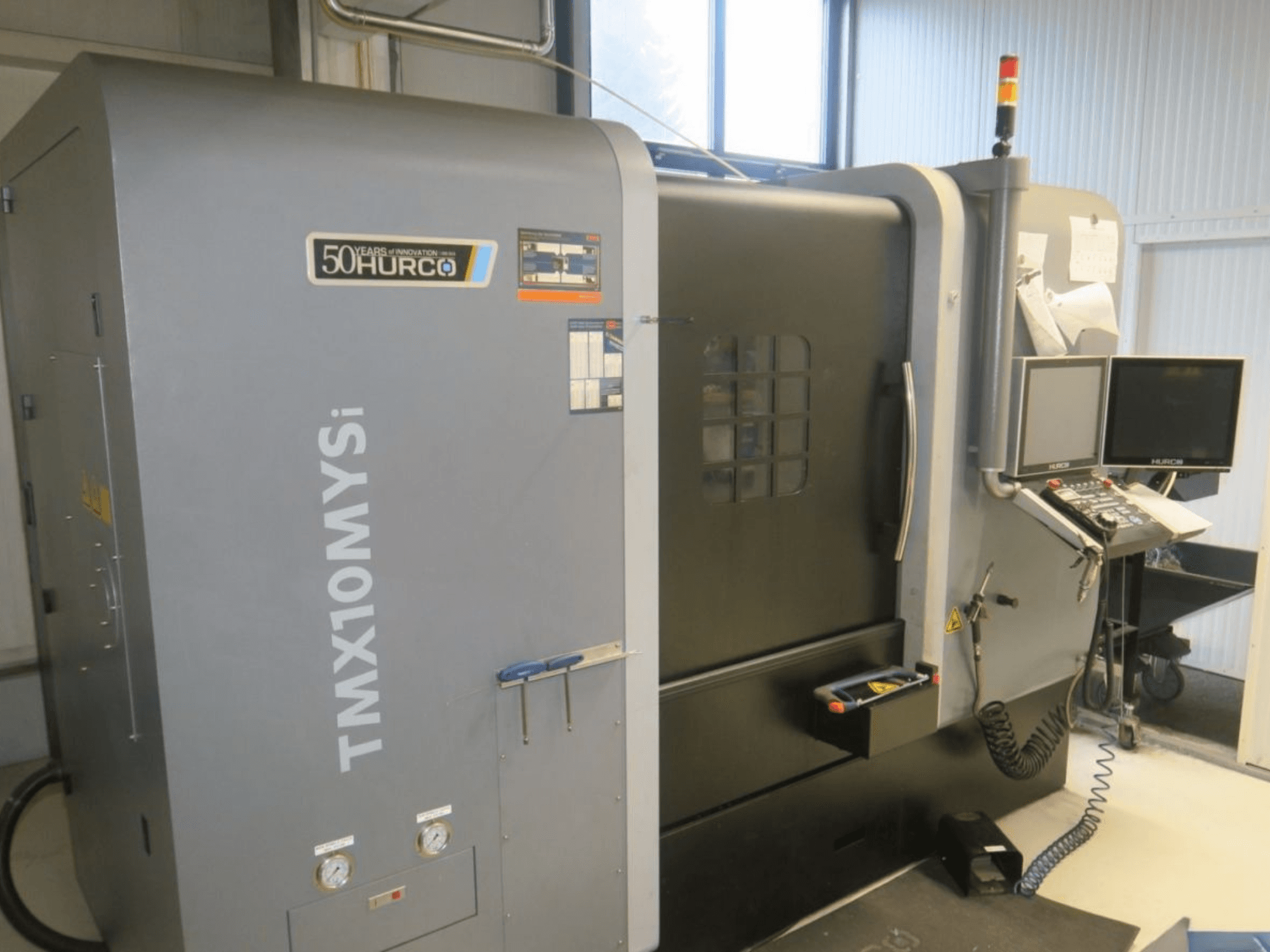 Hurco TMX10MYSi CNC mašīna sānu skatā; vadības panelis, avārijas gaismas un rādītāji.