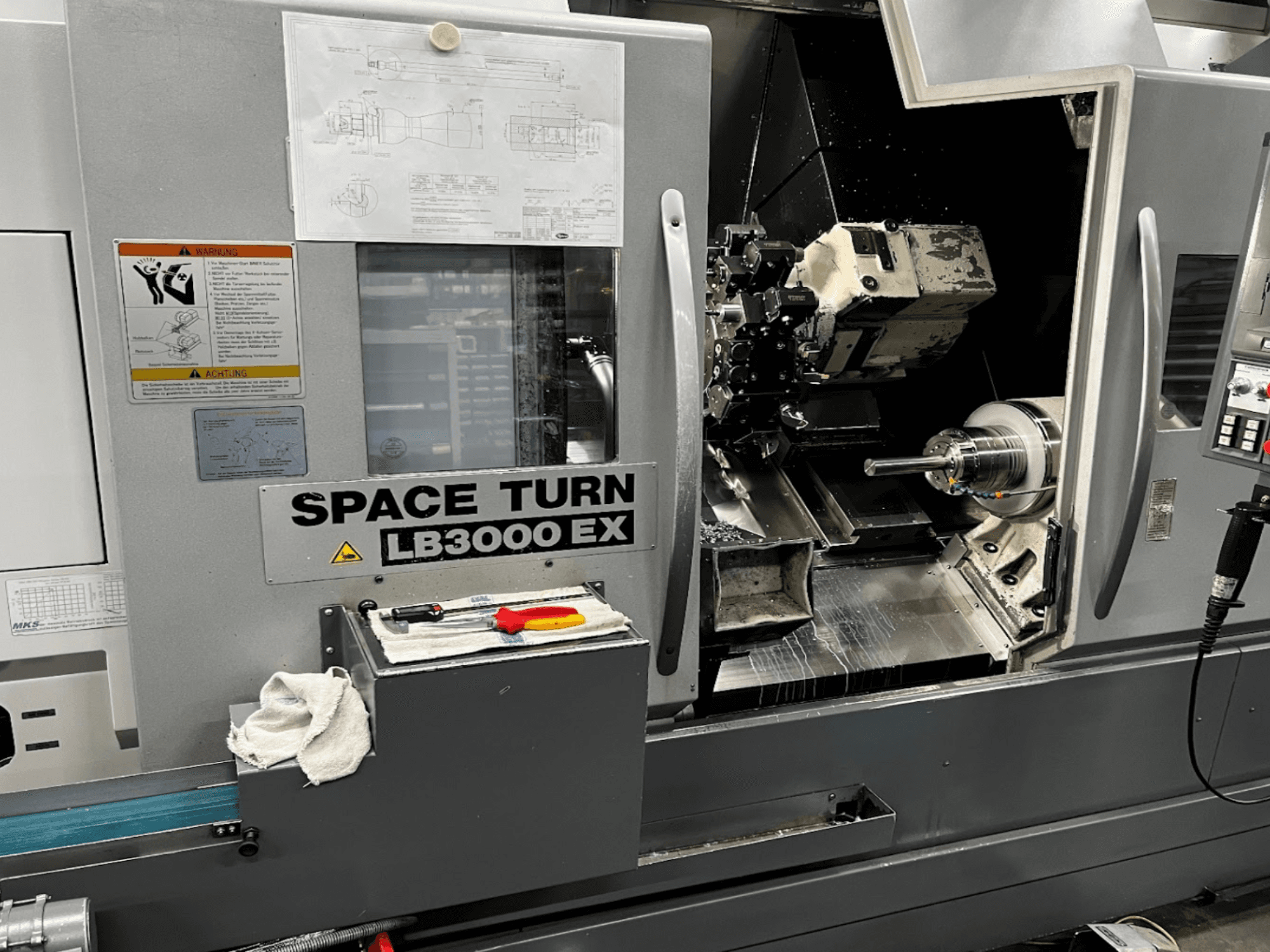 Okuma LB3000EX MYW horizontālās virpošanas darbgalds, priekšējais skats ar redzamu vadības paneli, instrumentiem un darba vietas detaļām.