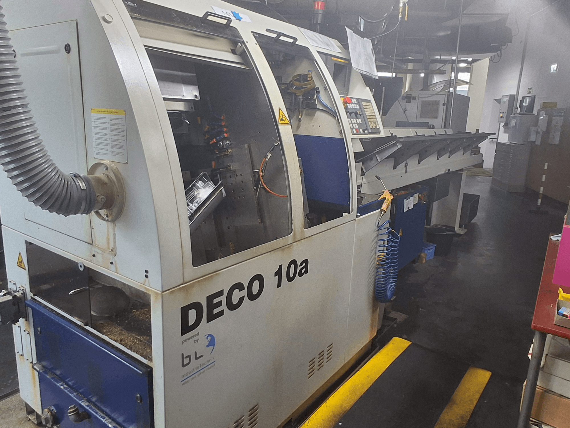 Šveices tipa virpmašīna TORNOS DECO 10a, skats no priekšpuses; vadības panelis, redzami mehānismi un putekļu nosūces caurule.