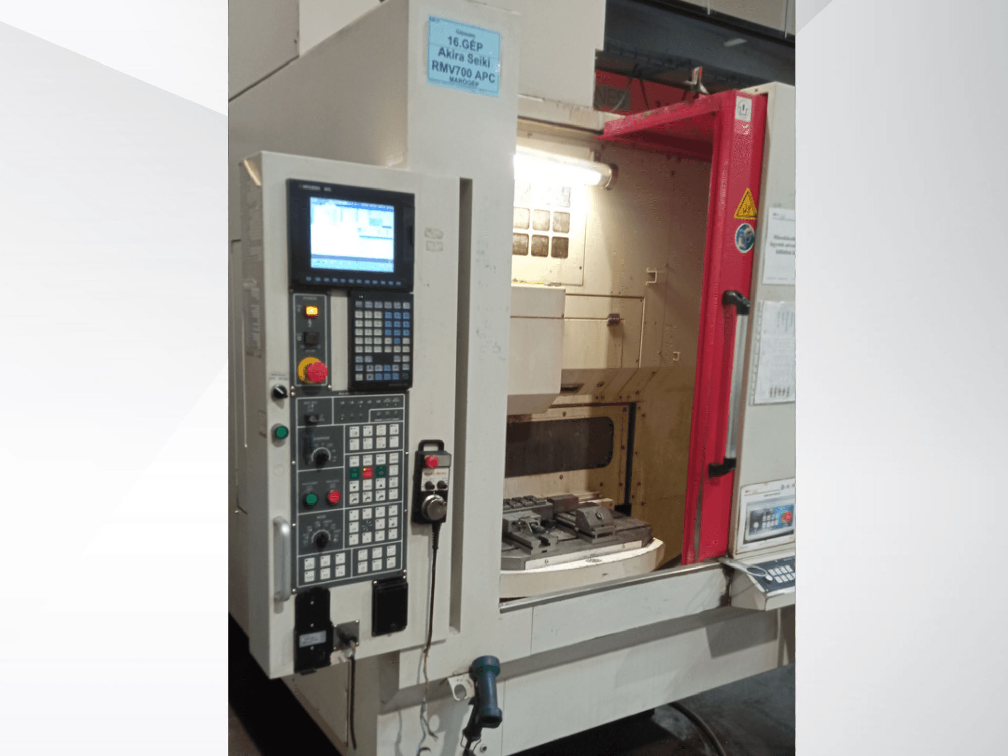 Akira Seiki RMV 700 APC vertikālais apstrādes centrs no priekšpuses ar digitālo vadības paneli un darba zonu ar instrumentiem.