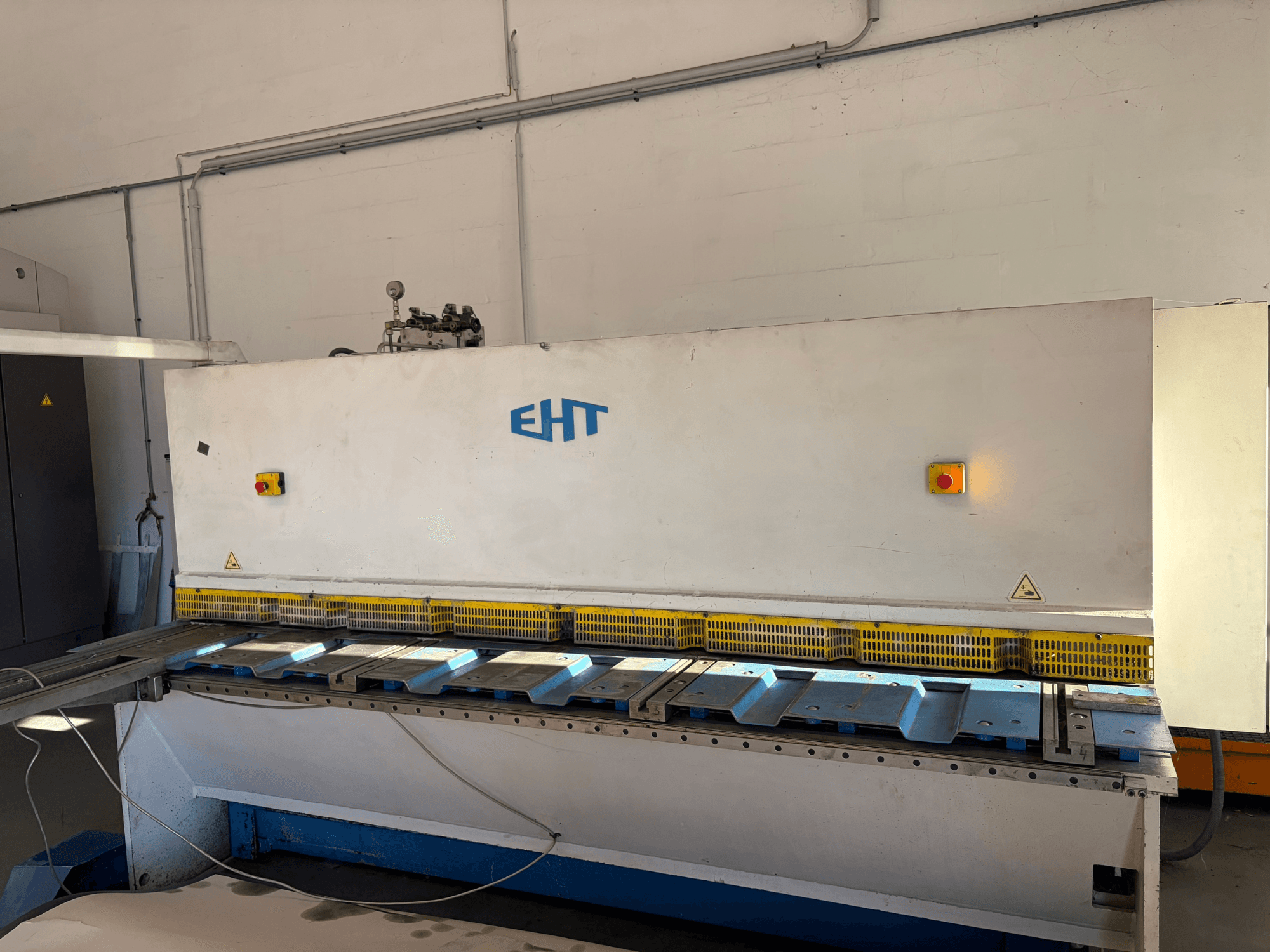 Hidrauliskā griešanas mašīna EHT ISS 5-30 darbnīcā, skats no priekšpuses, kurā redzams vadības panelis un griešanas virsma.