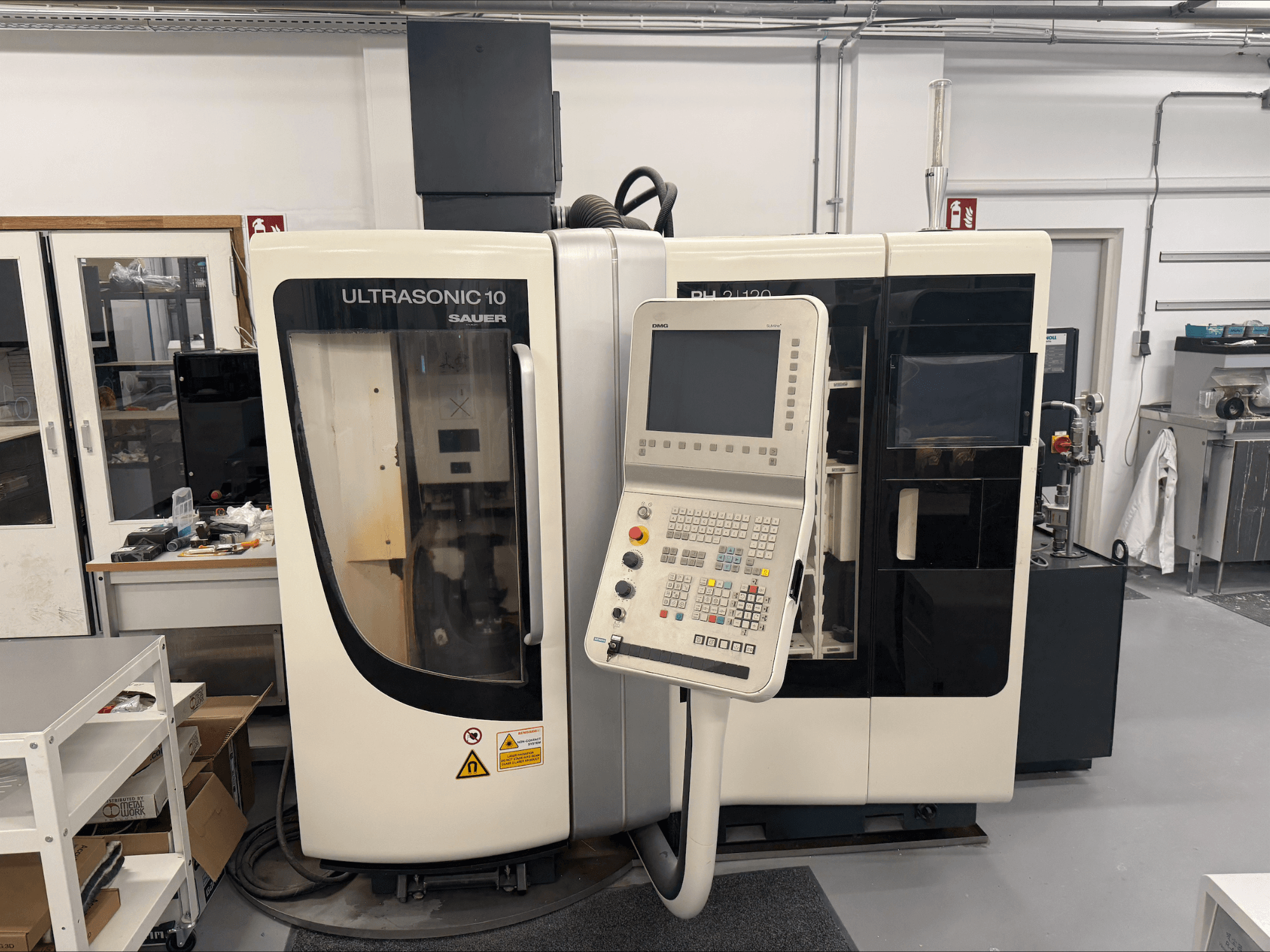 DMG Sauer Ultrasonic 10 + PH 2 | 120 vertikālais apstrādes centrs, skats no priekšpuses, ar vadības paneli un lielu skatu logu.