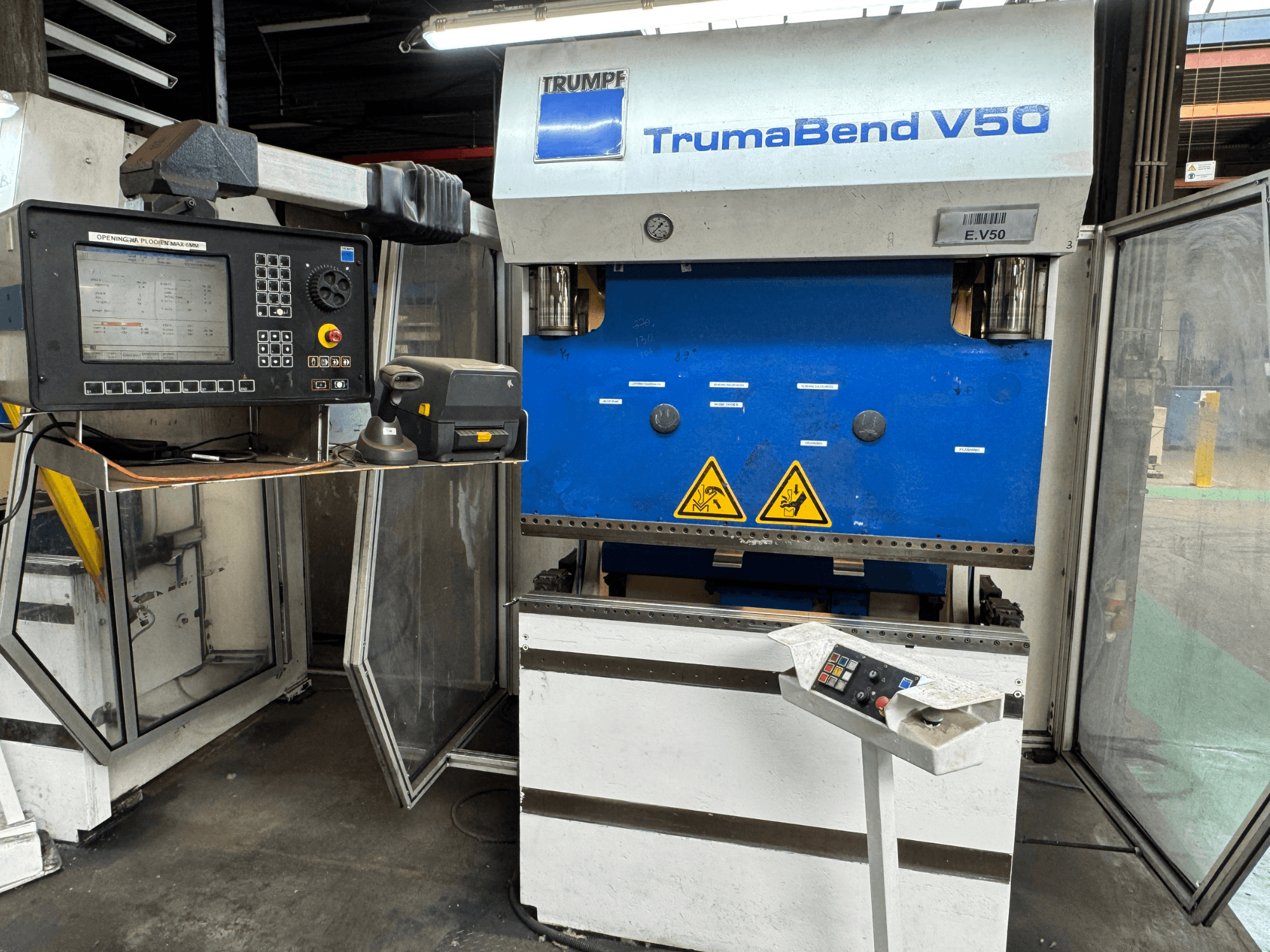 TRUMPF TrumaBend V50 preses bremze no priekšpuses, ar vadības paneli, drošības brīdinājumiem un izteiktu zili baltu dizainu.